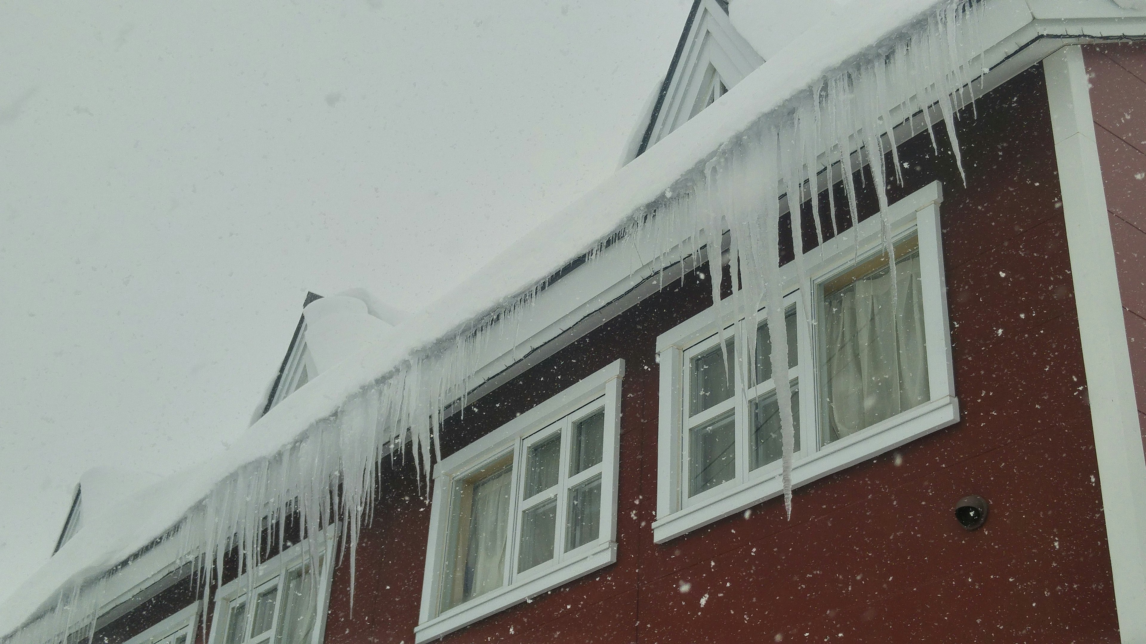 雪に覆われた赤い家の屋根に氷柱が垂れ下がっている