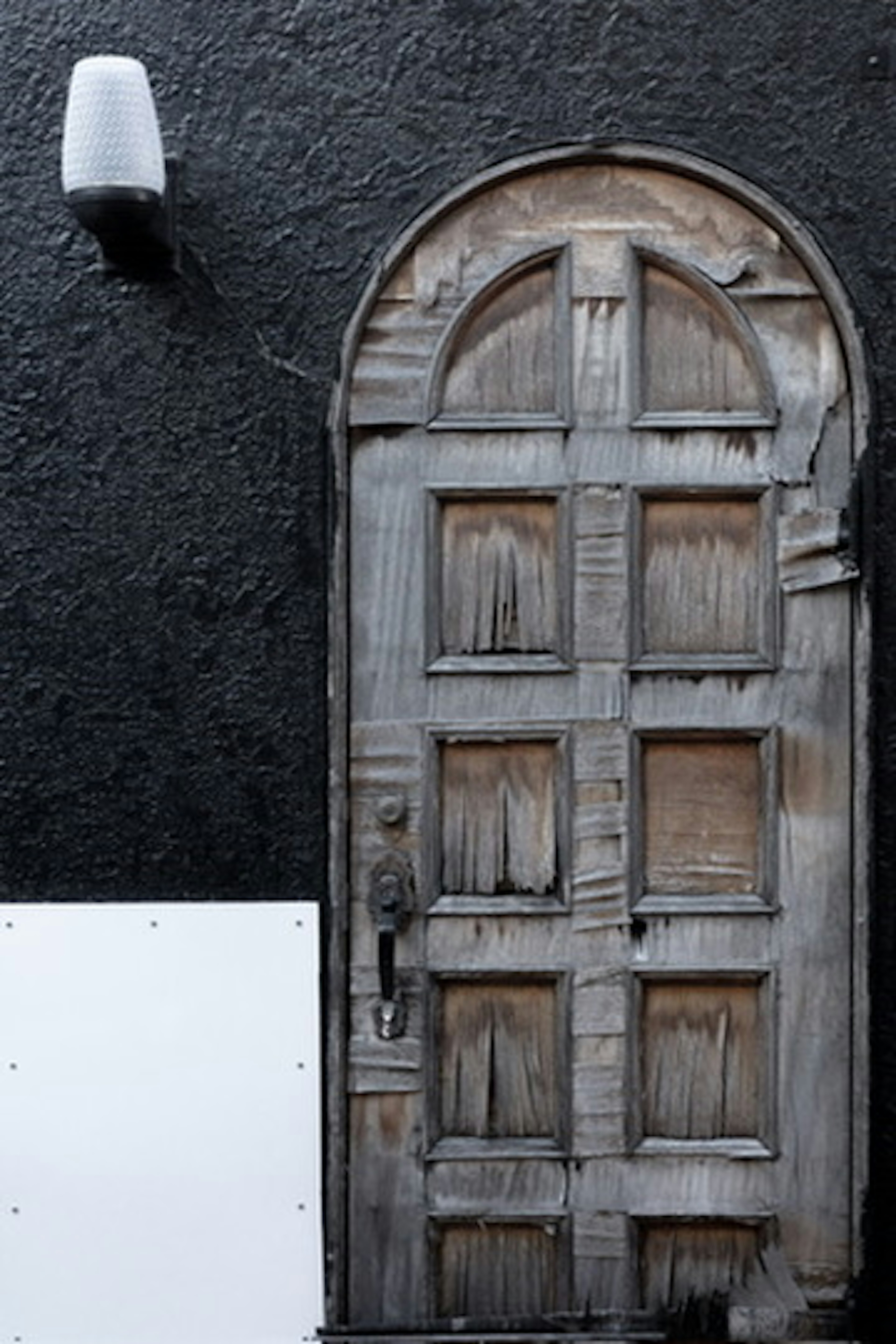 An aged wooden arched door mounted on a black wall