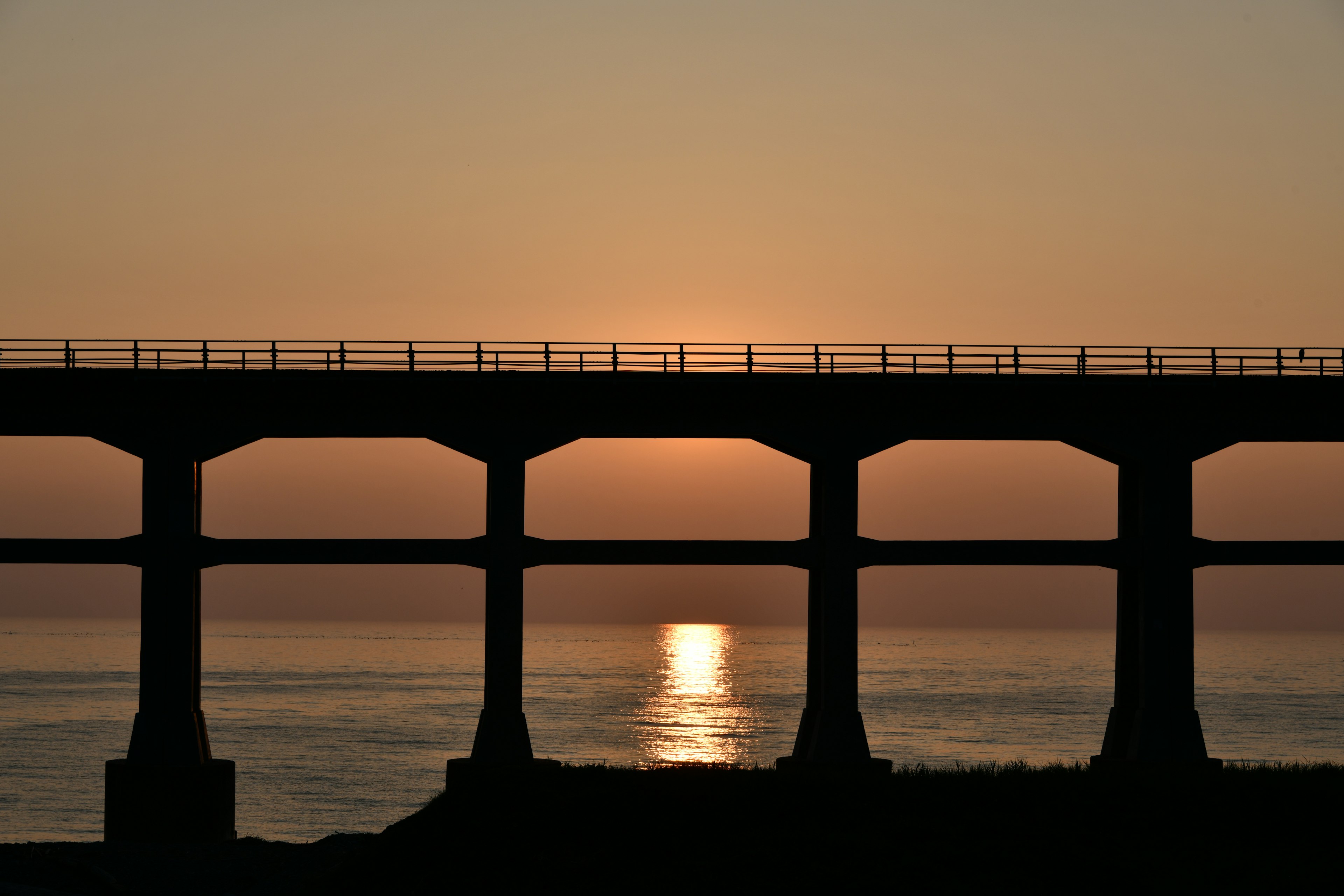 Silhouette di un ponte contro un tramonto che si riflette sul mare