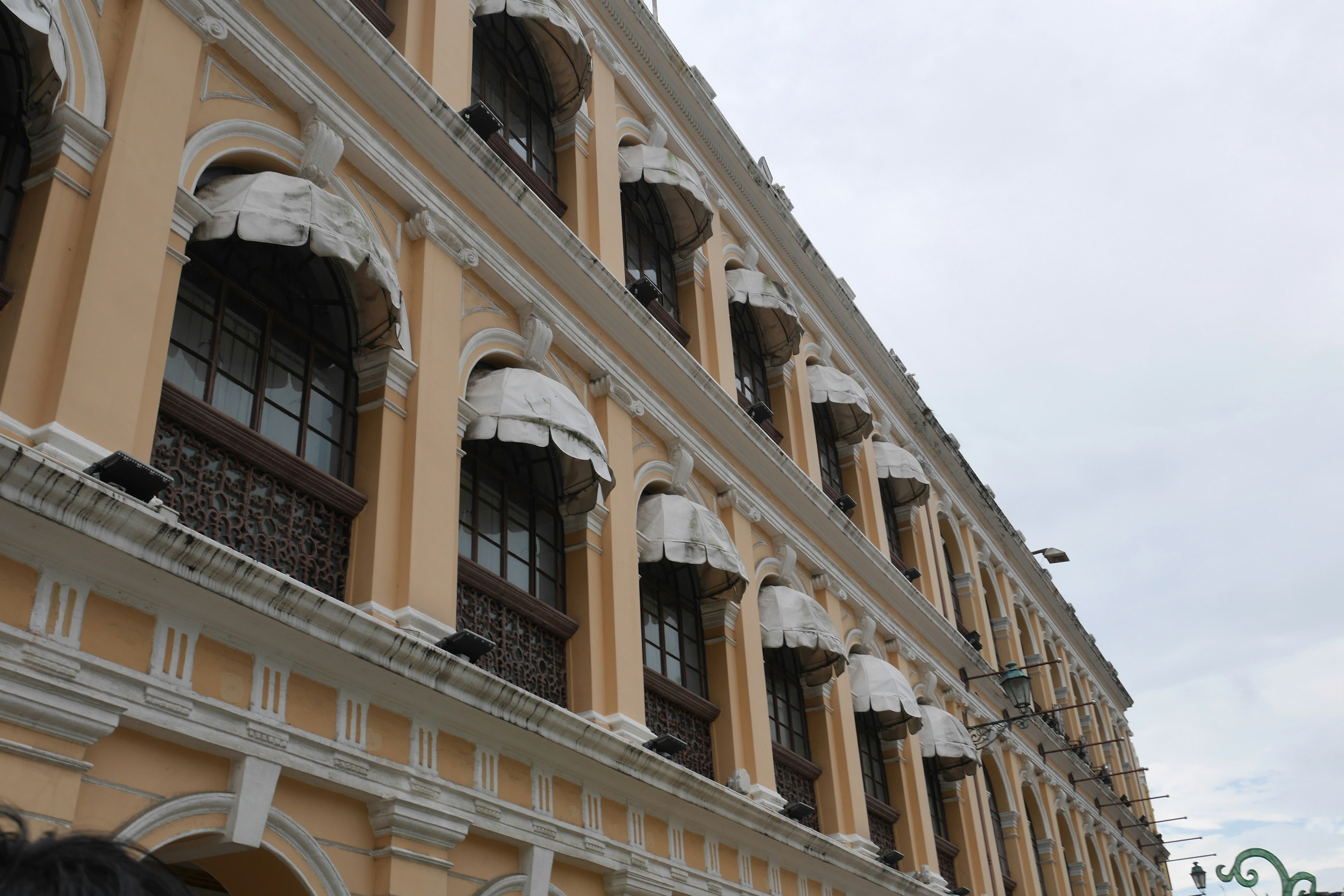 Fachada de un edificio de estilo clásico con toldos blancos sobre las ventanas y distintivas paredes amarillas