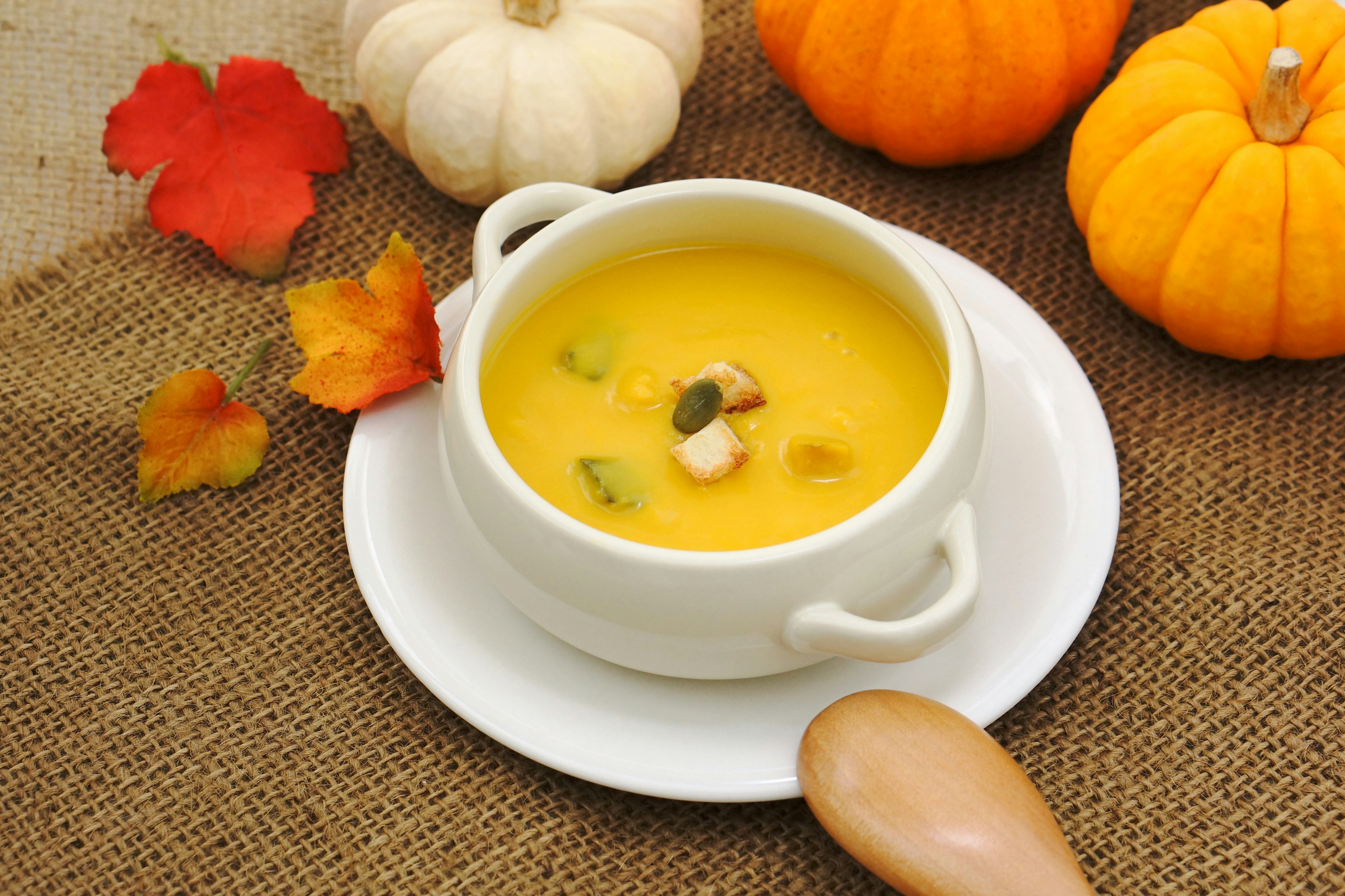 Soupe de potiron crémeuse servie dans un bol blanc entouré de citrouilles orange et de feuilles d'automne