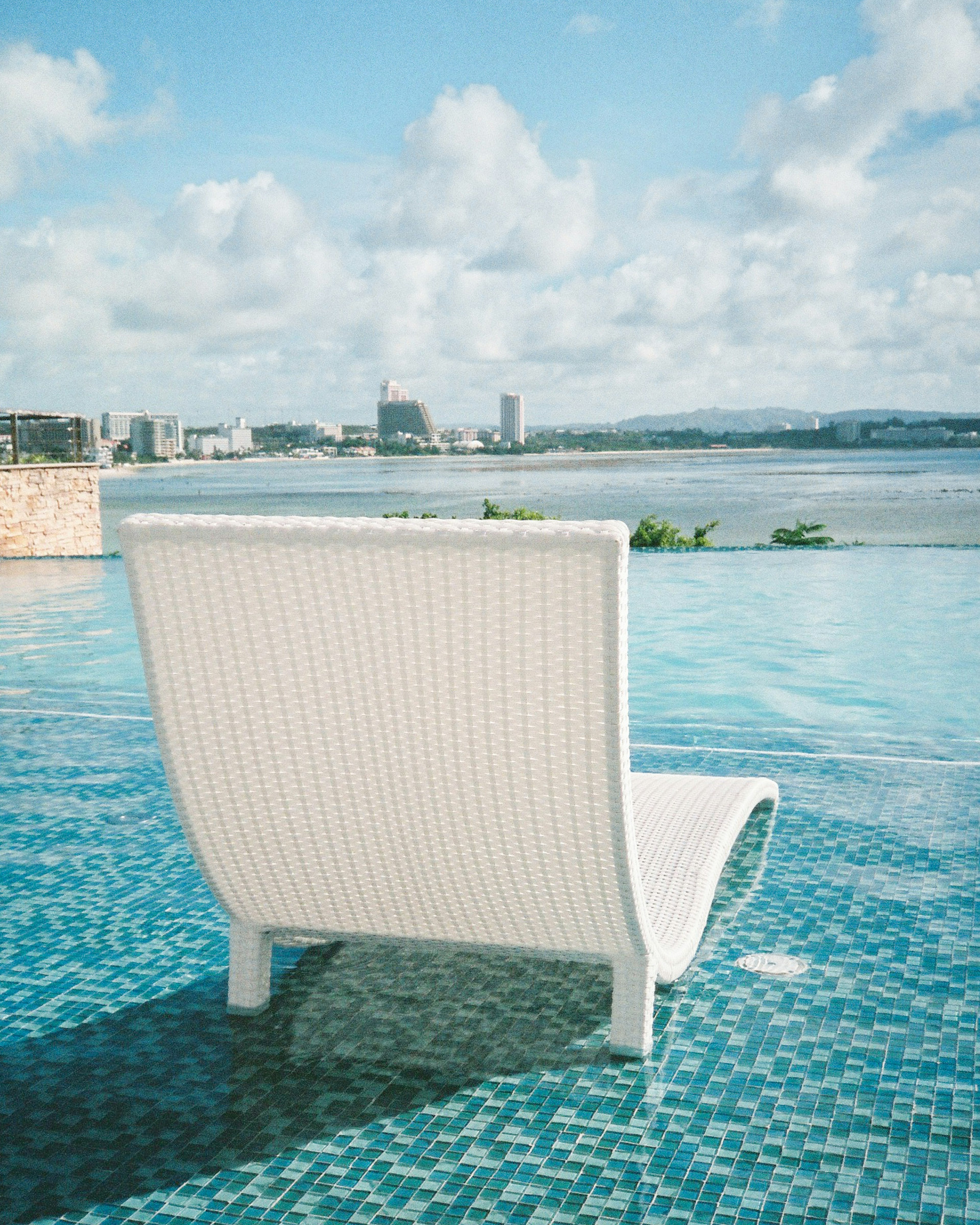 Ein weißer Liegestuhl neben einem blauen Swimmingpool mit wunderschönem Meerblick im Hintergrund