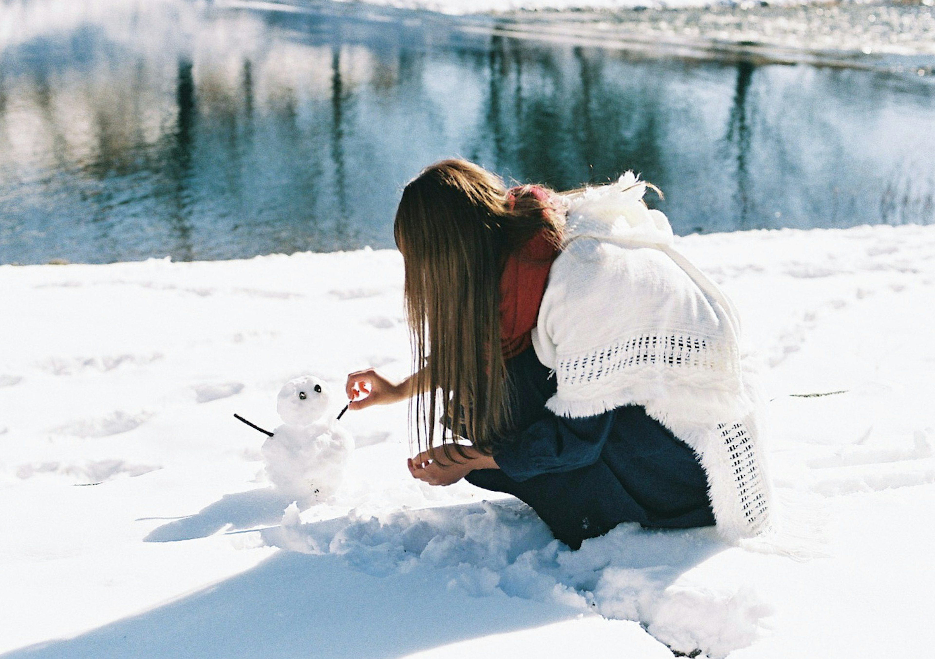 在河边的雪中堆雪人的女人