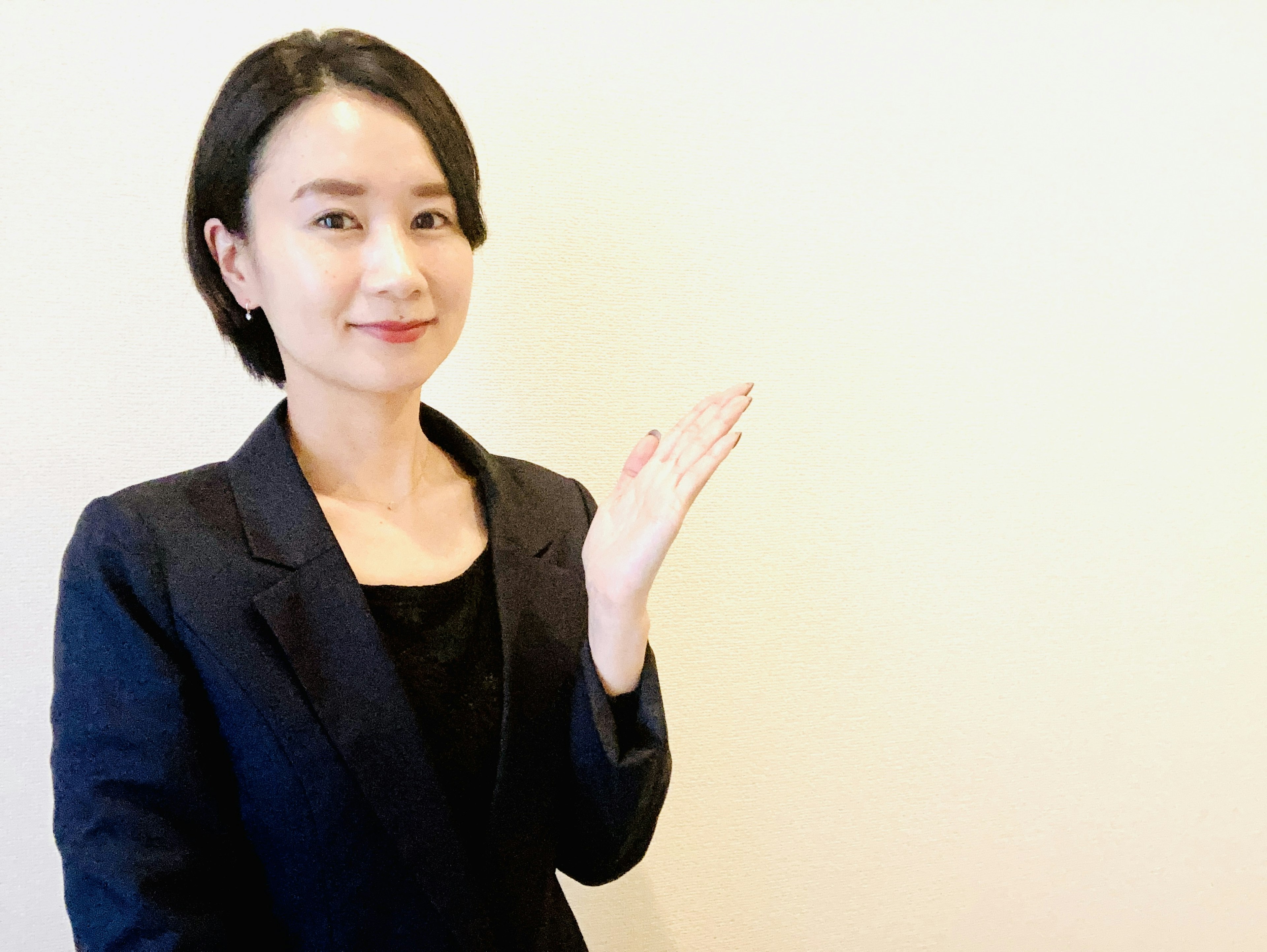 A woman in a business suit gesturing with her hand against a plain background