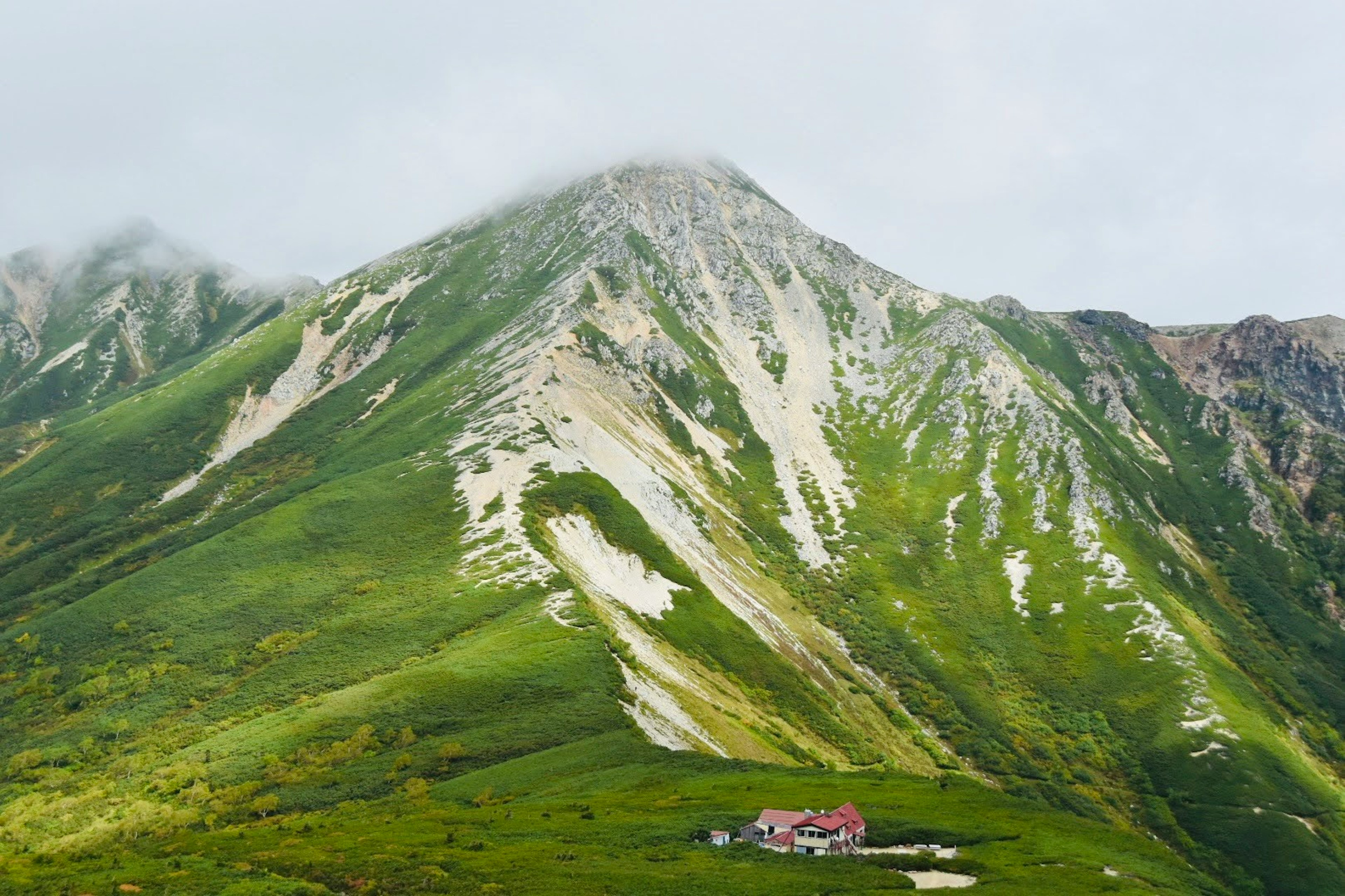 緑の山と雲に覆われた山頂に小さな家がある風景