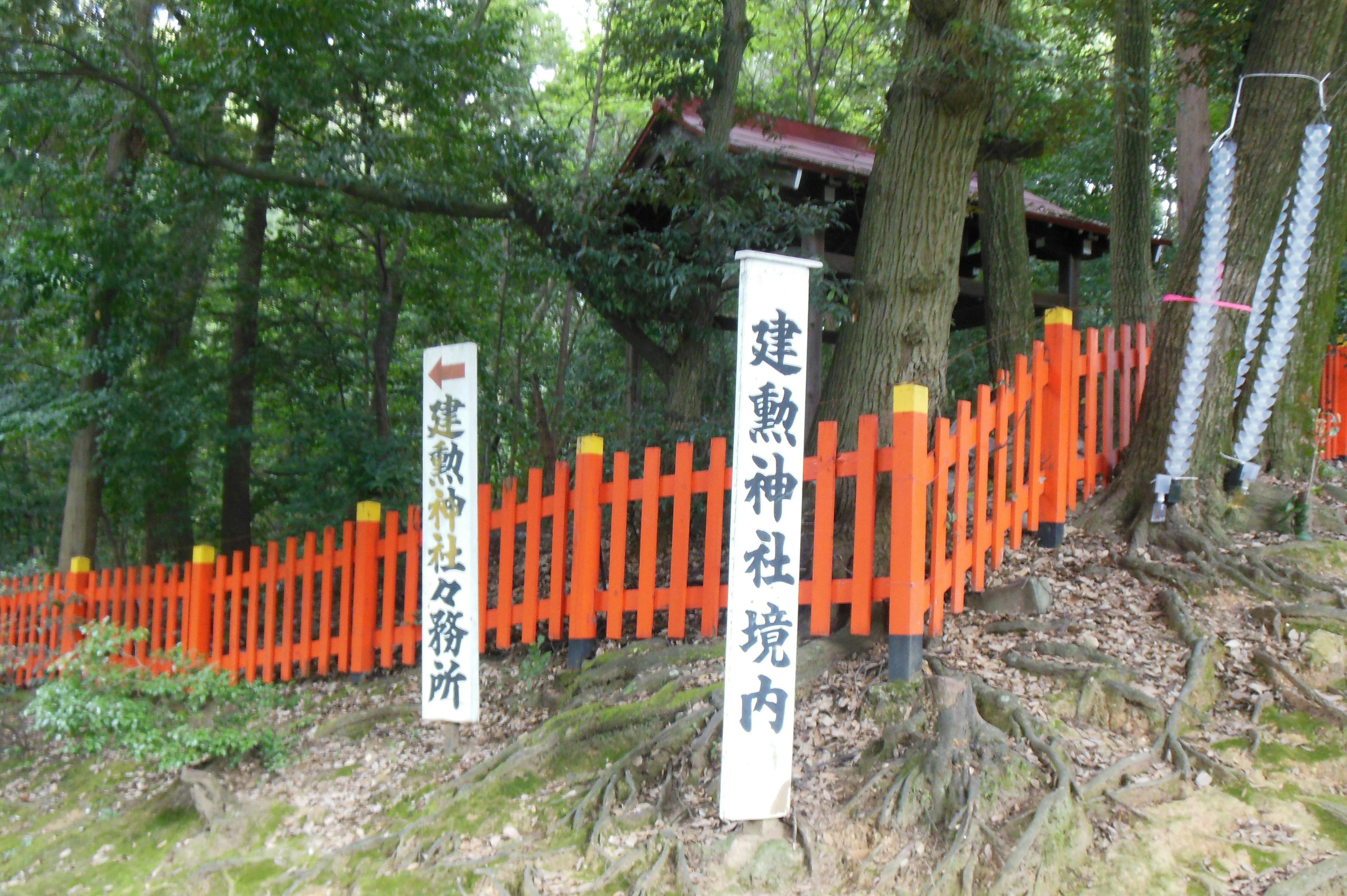 緑の木々に囲まれた朱色のフェンスと神社の標識