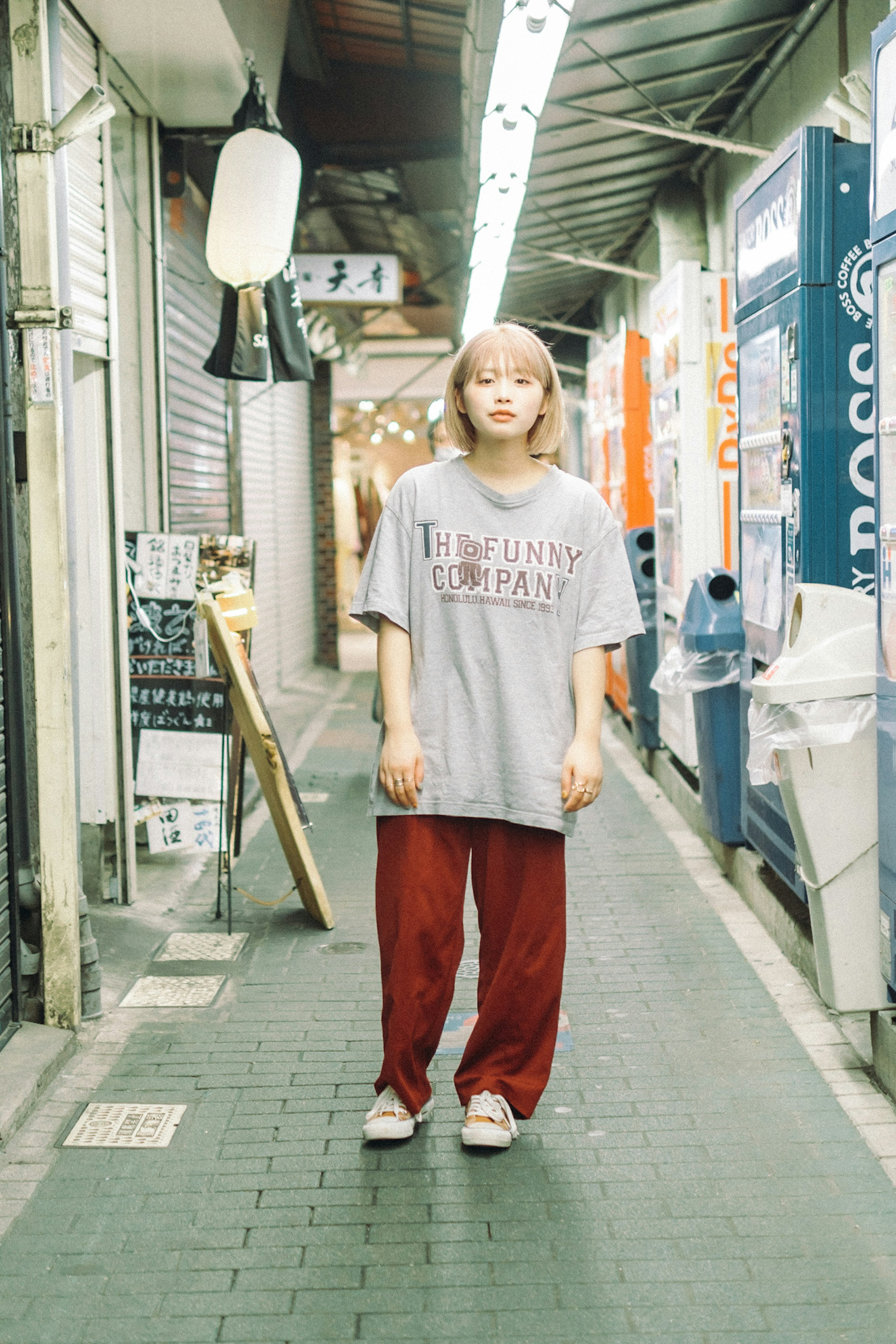 狭い通りに立つ女性がグレーのTシャツと赤いパンツを着ている