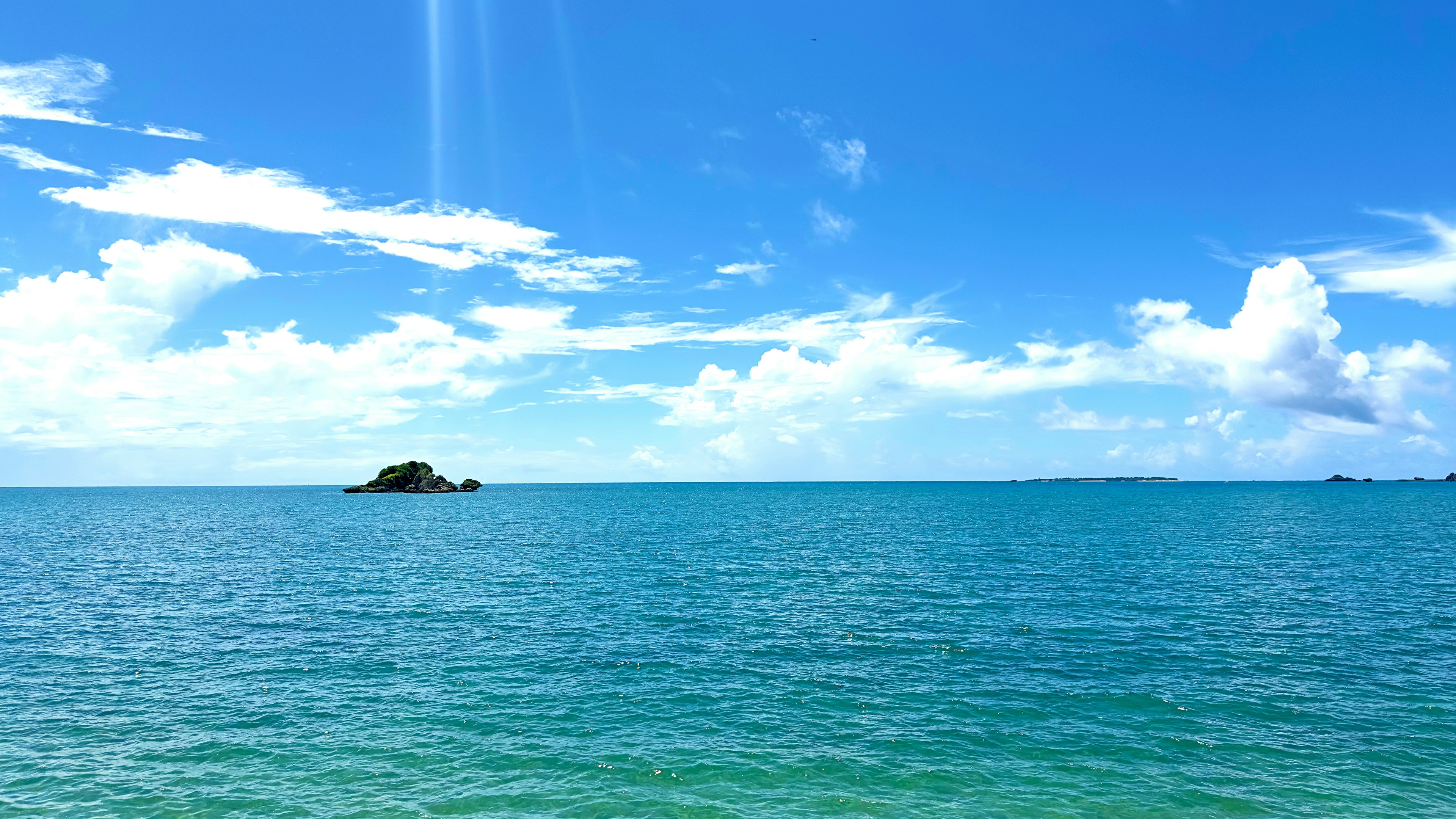 A scenic view of blue ocean and sky with a small island in the distance