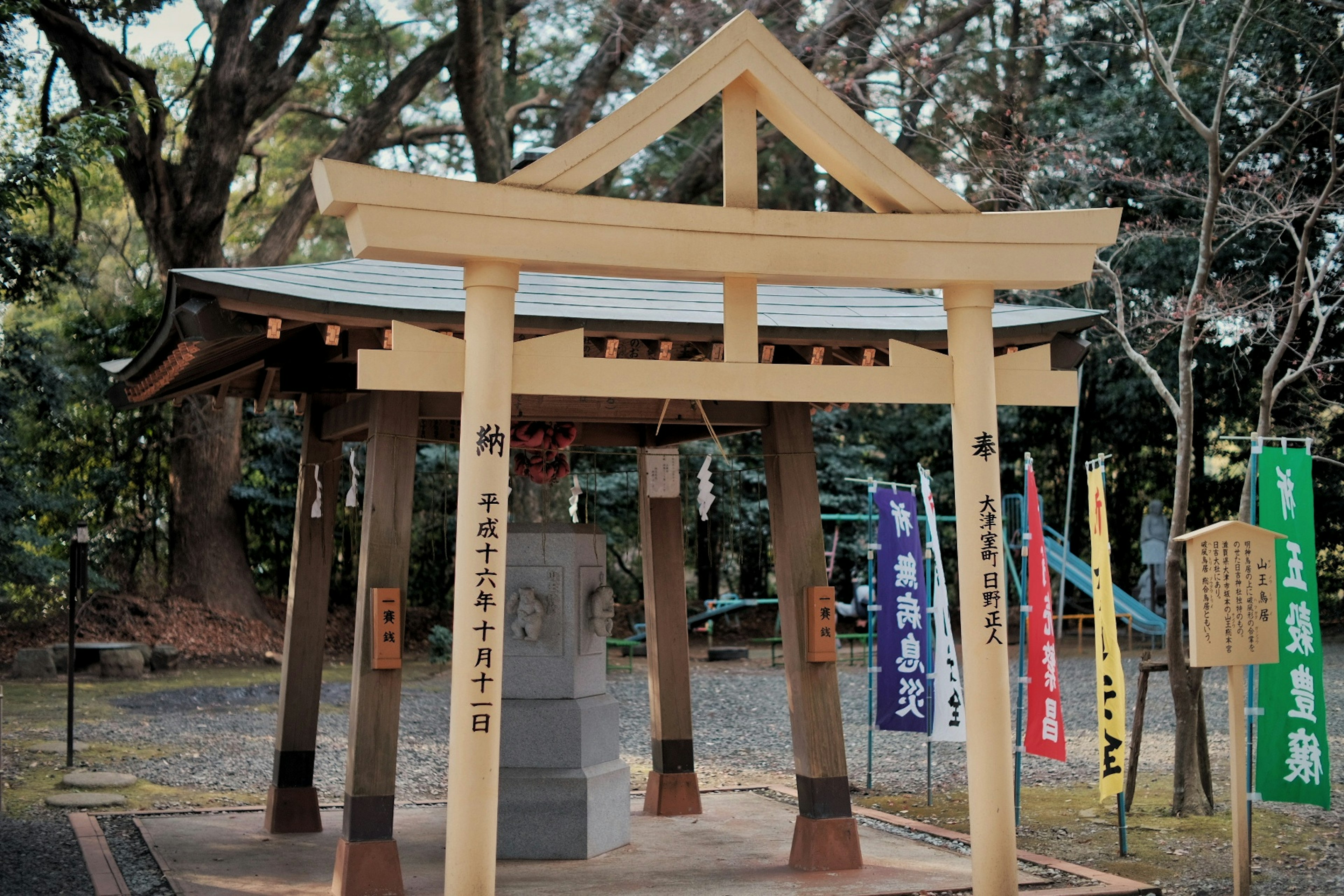 Vista escénica de un santuario con una puerta torii de madera y una campana rodeada de pancartas coloridas