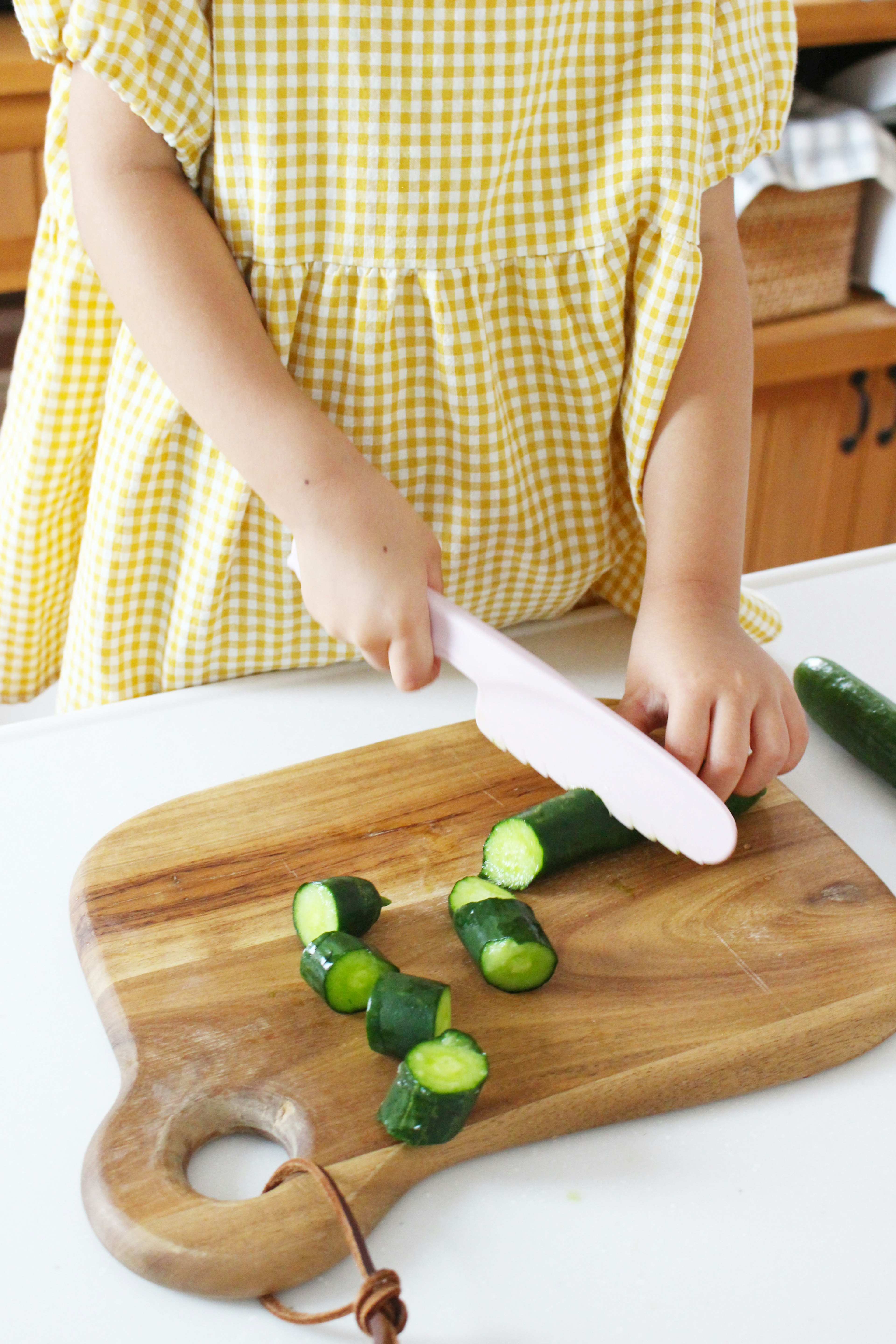 Child slicing cucumbers on a wooden cutting board