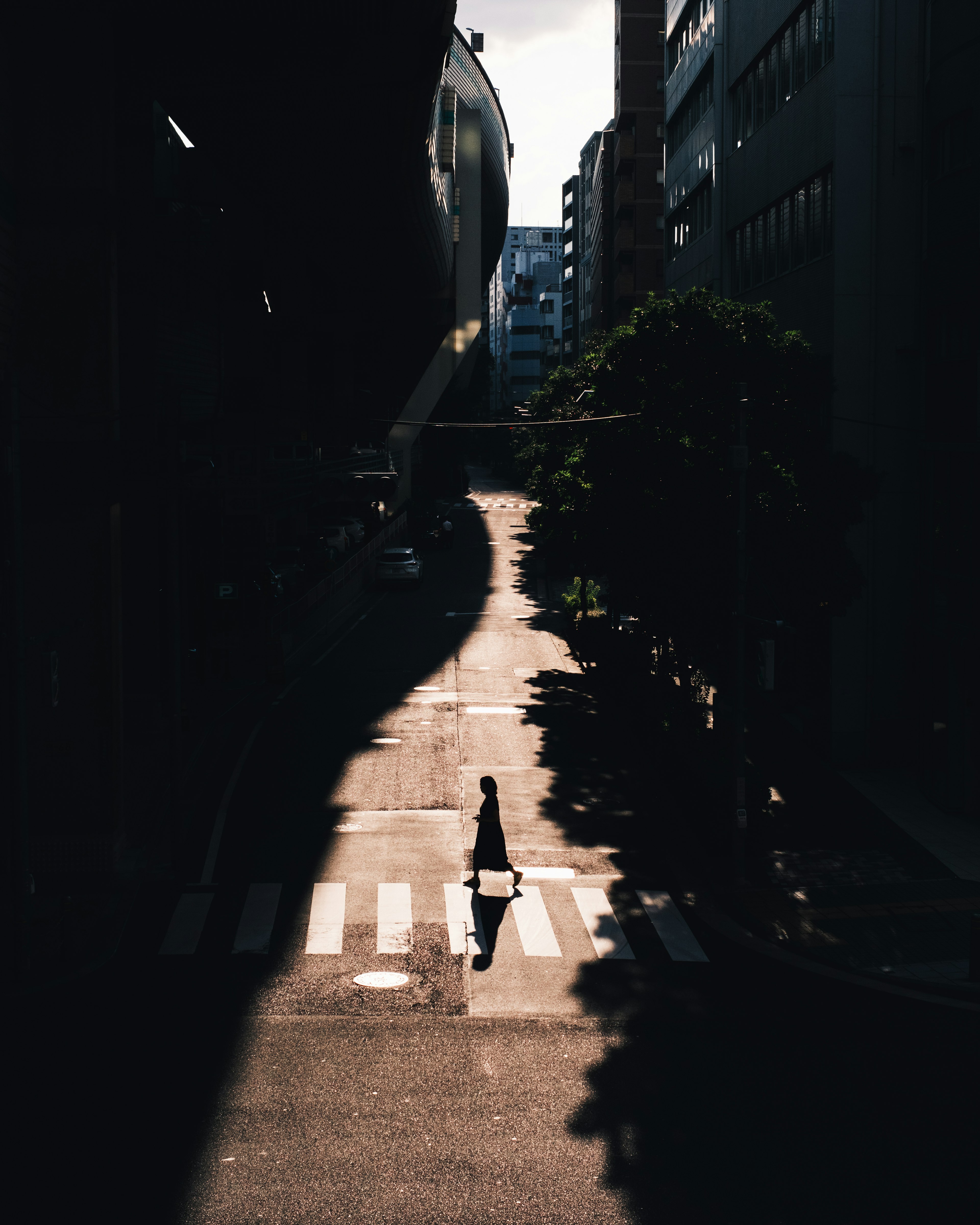 A silhouette of a person walking on a quiet street with shadows