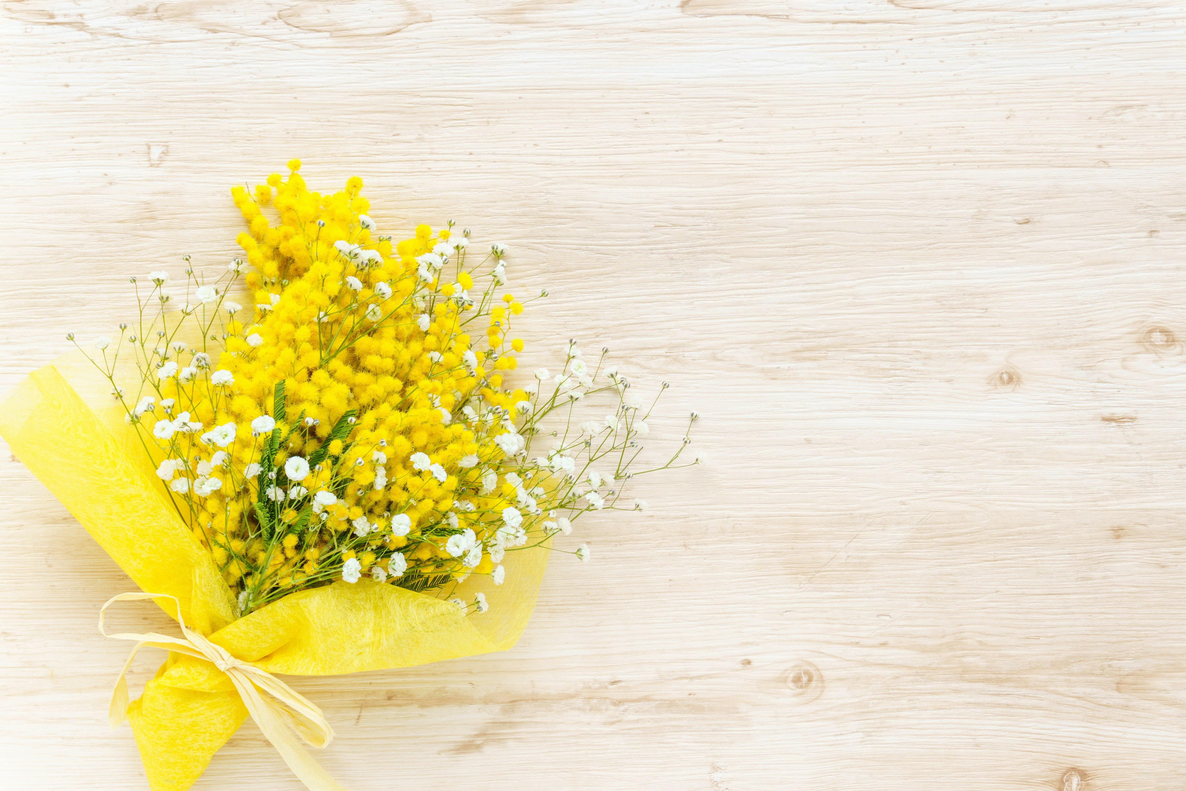 A bouquet of yellow mimosa and white flowers wrapped in yellow paper on a wooden table