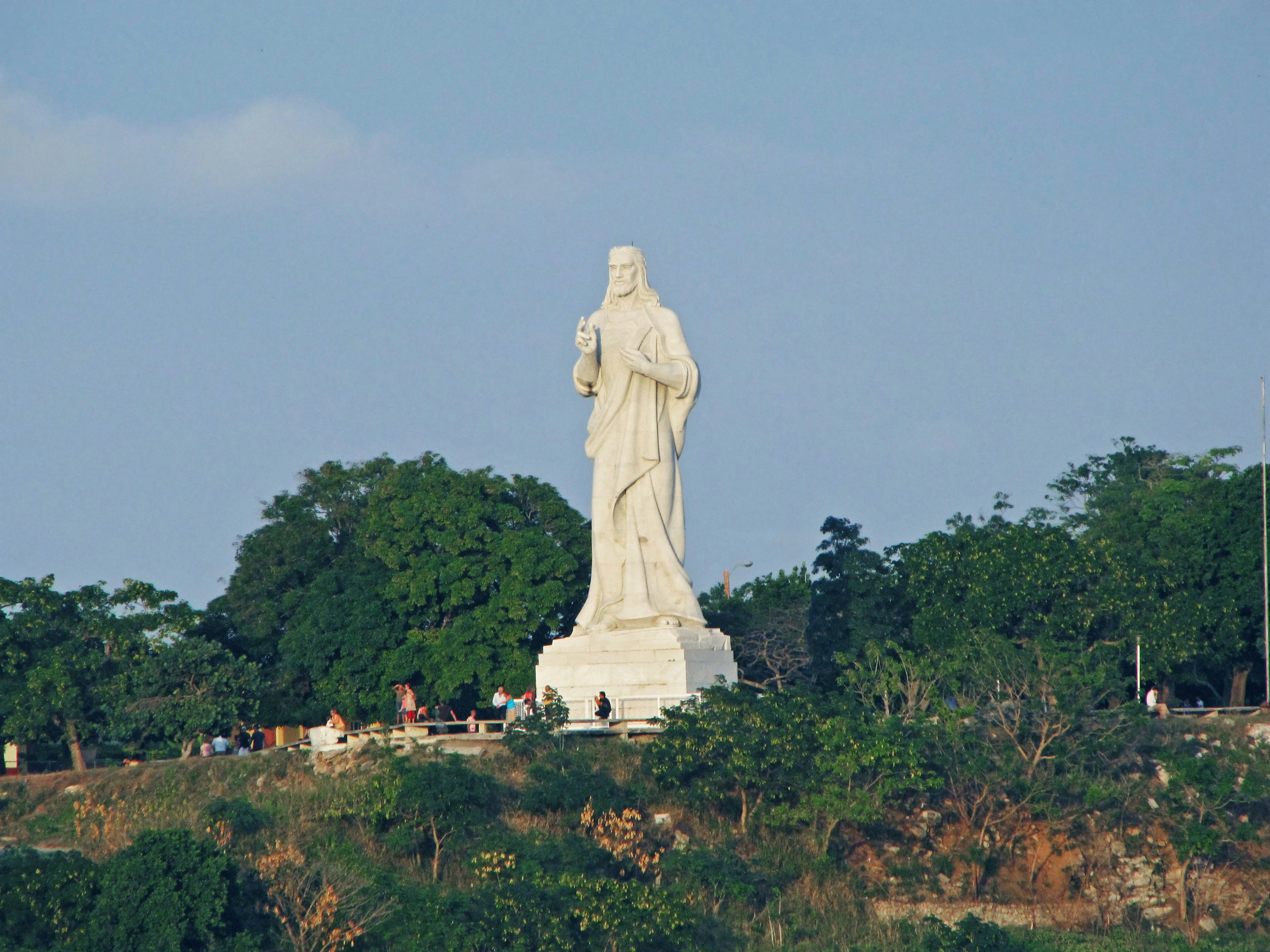 Una grande statua bianca che si erge su una collina circondata da alberi verdi