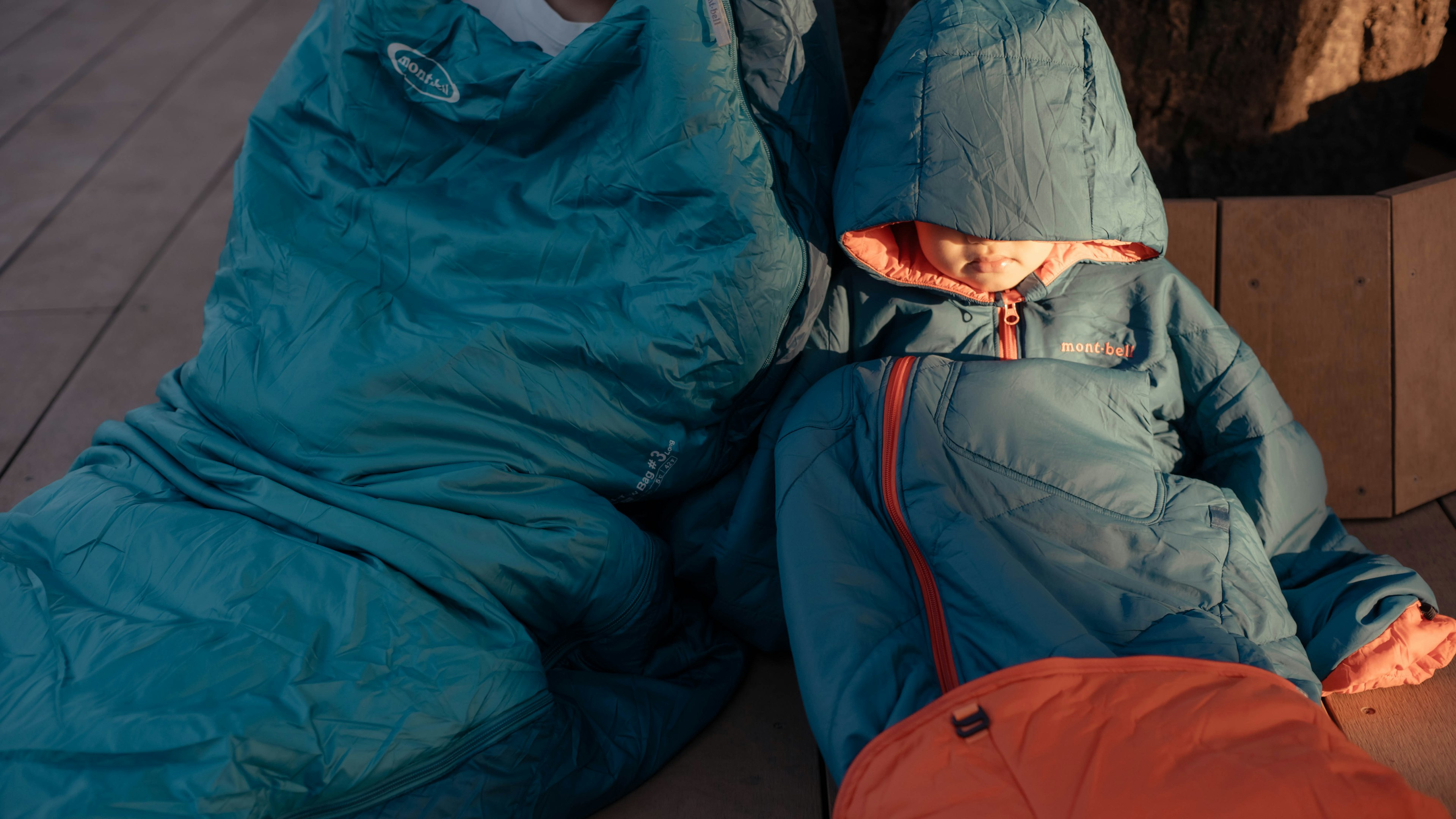 Two children resting in blue sleeping bags on a wooden surface