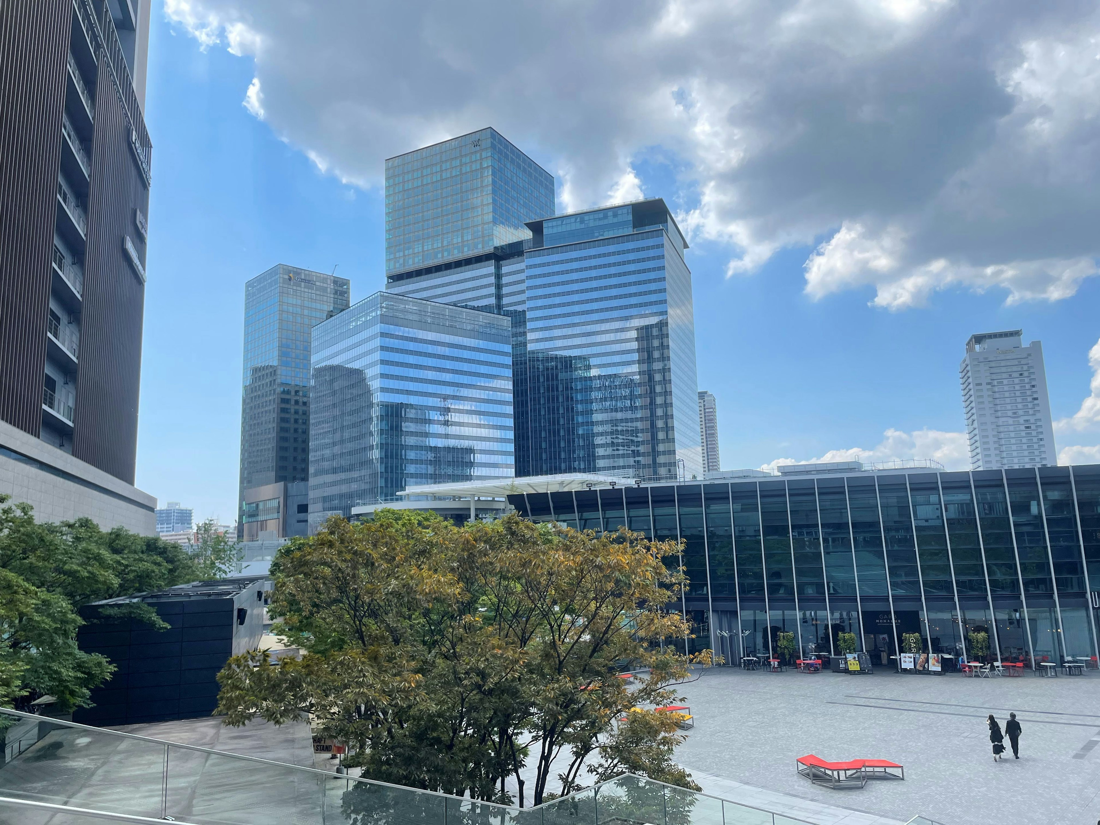 Garis langit perkotaan dengan gedung pencakar langit modern dan plaza terbuka di bawah langit biru