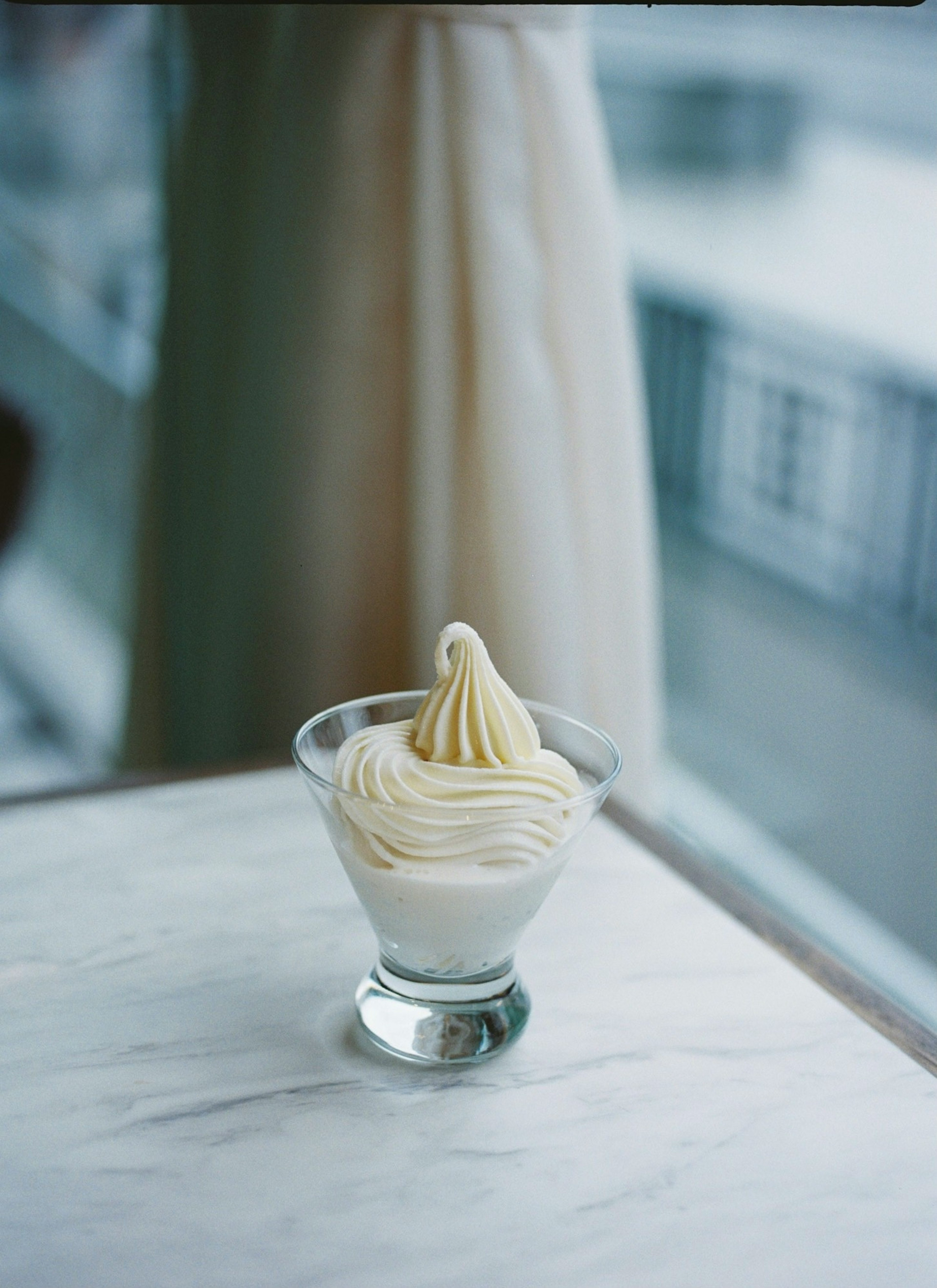 Une coupe de dessert avec de la crème blanche est placée sur une table près de la fenêtre