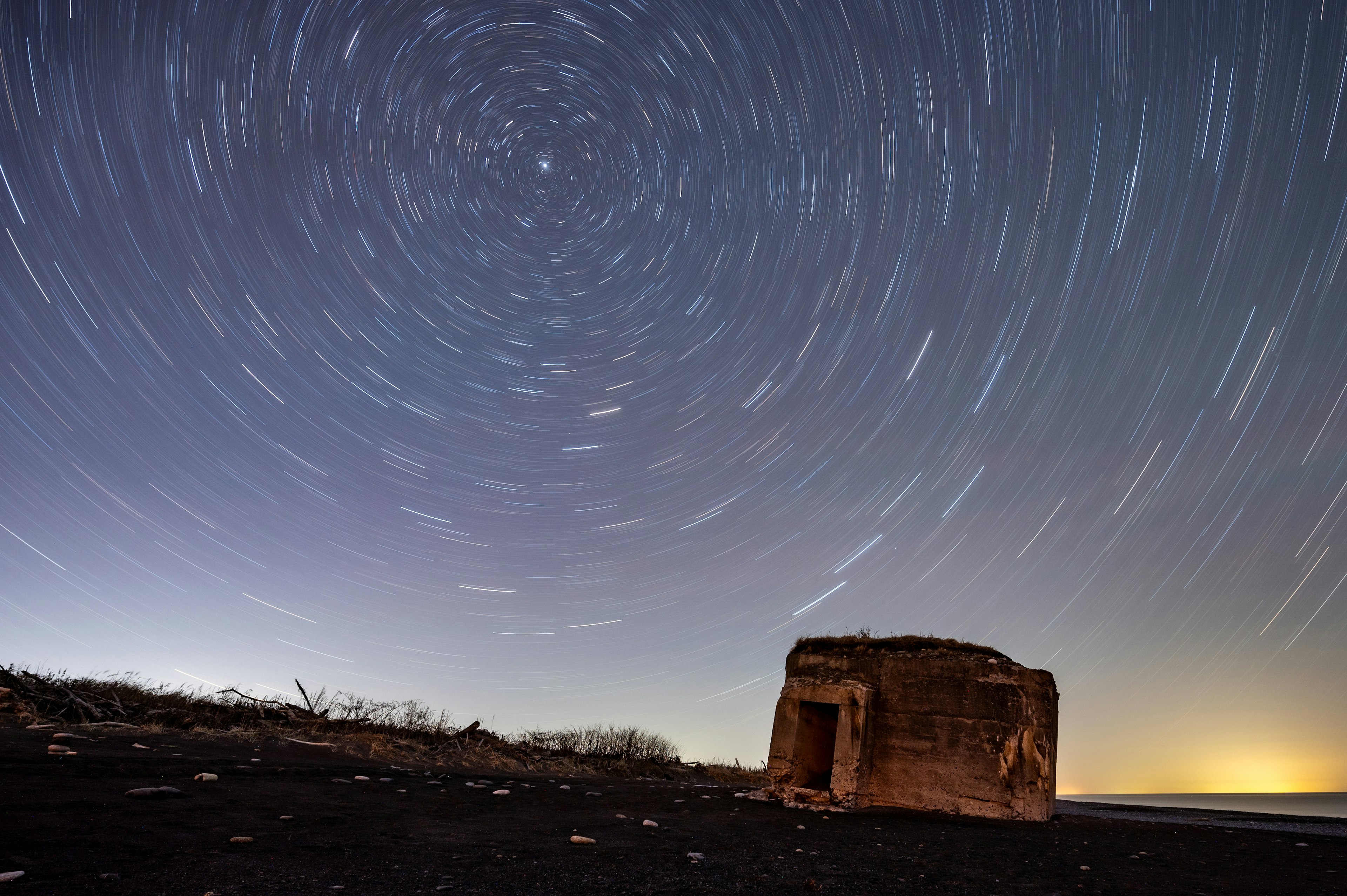 星の軌跡が描かれた夜空の下にある廃墟の建物