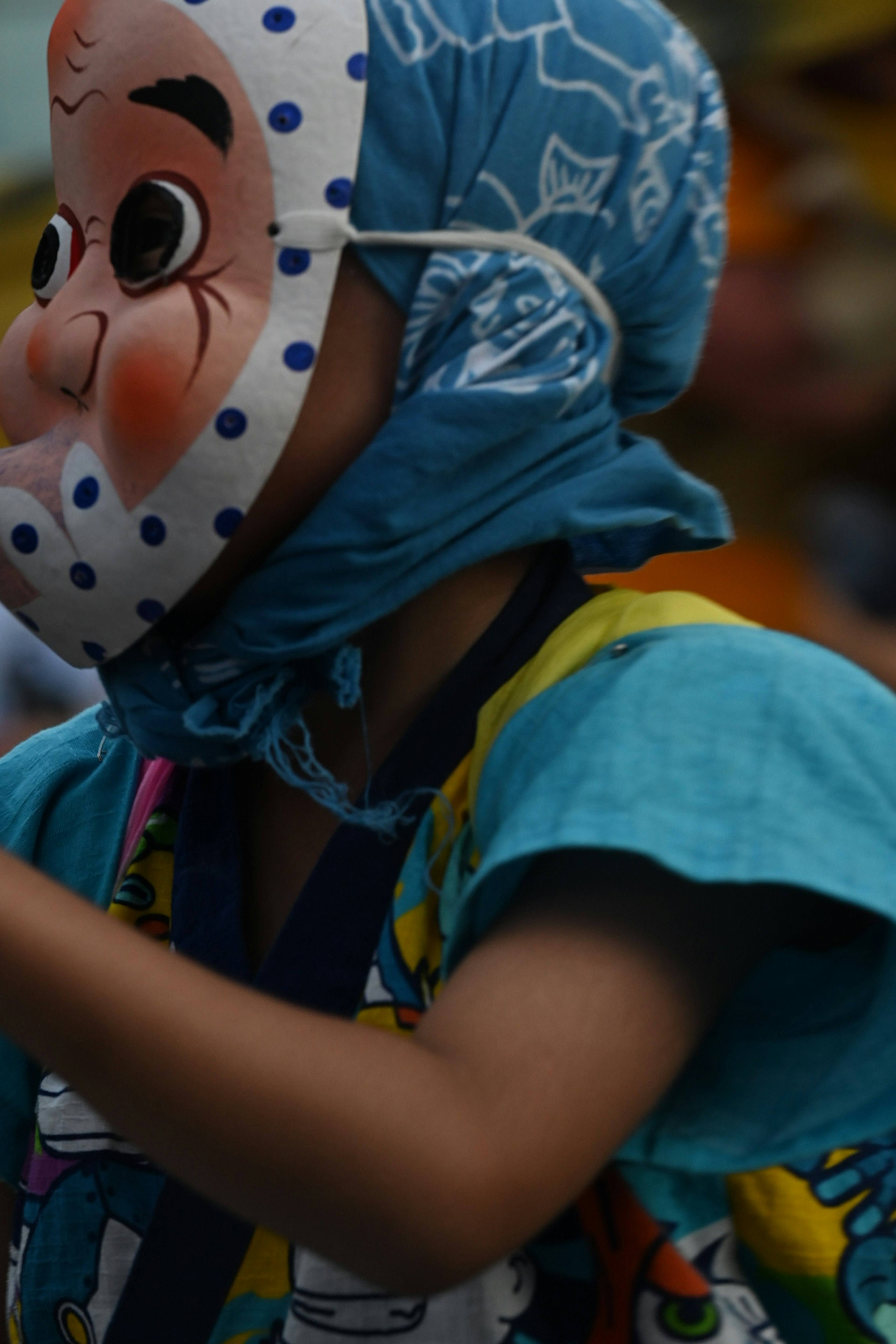 Child wearing a mask and blue outfit at a festival