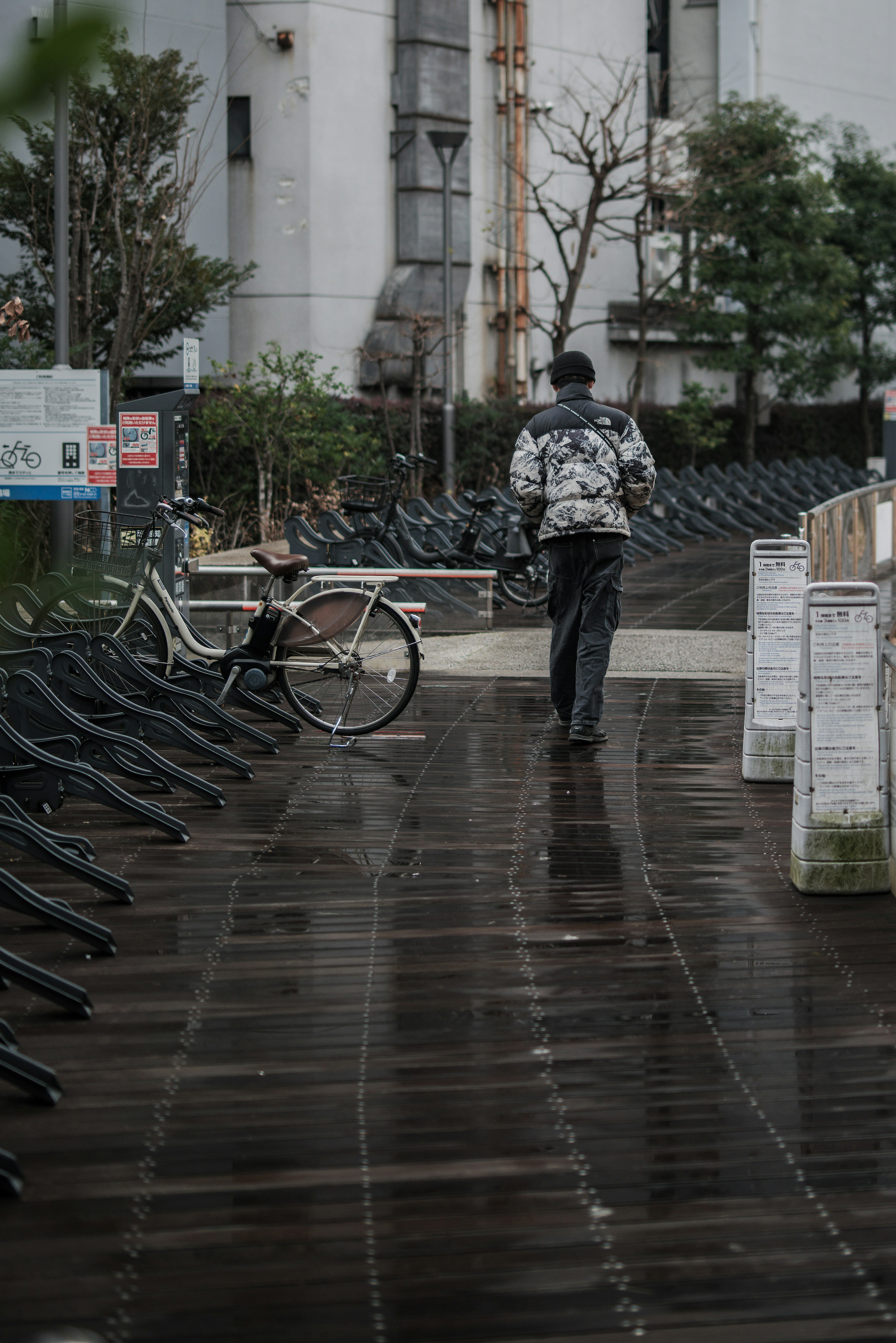 一个人在雨水淋湿的小路上走，附近有一辆自行车