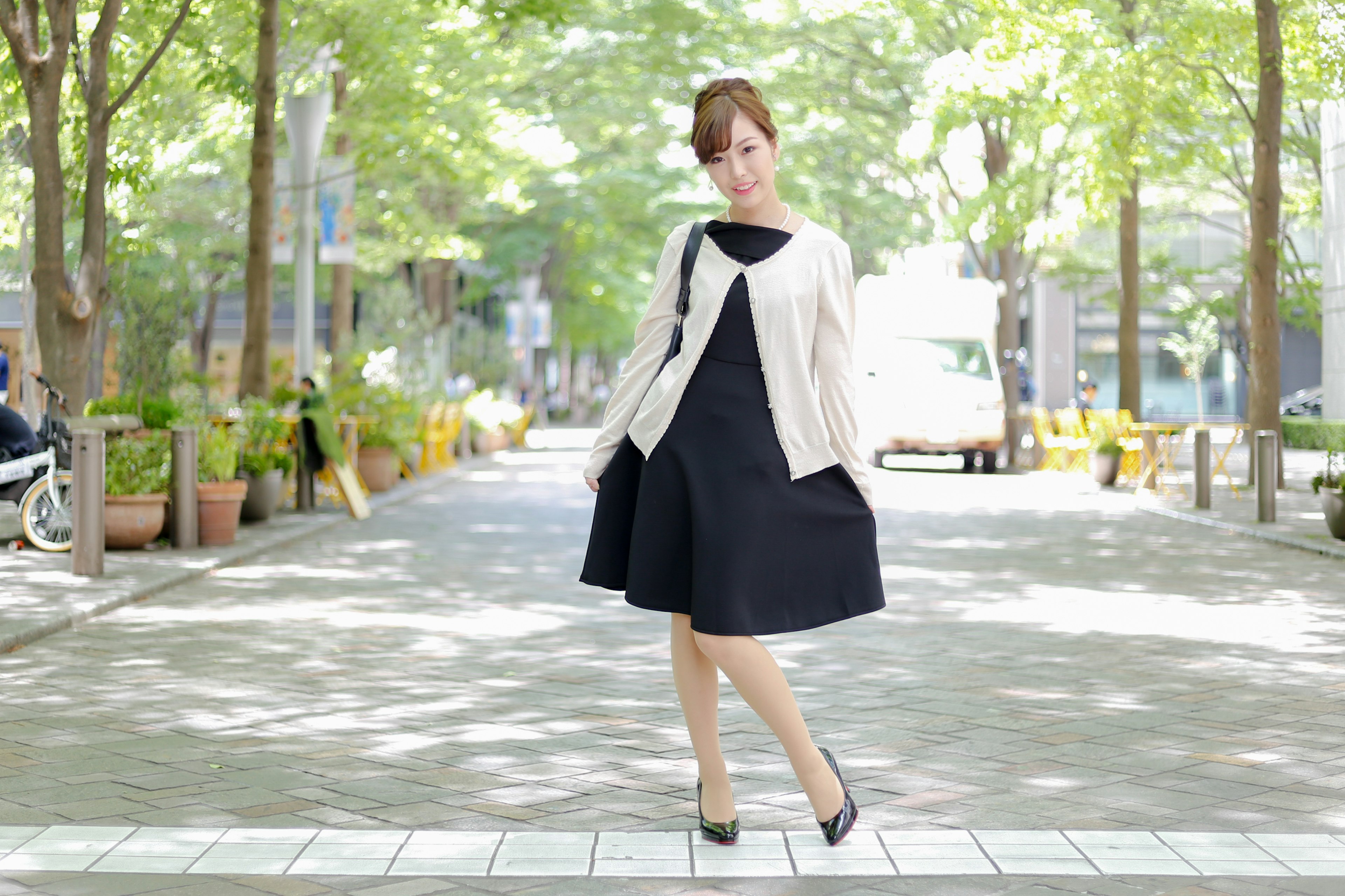 A woman in a black dress and white jacket walking on a park pathway