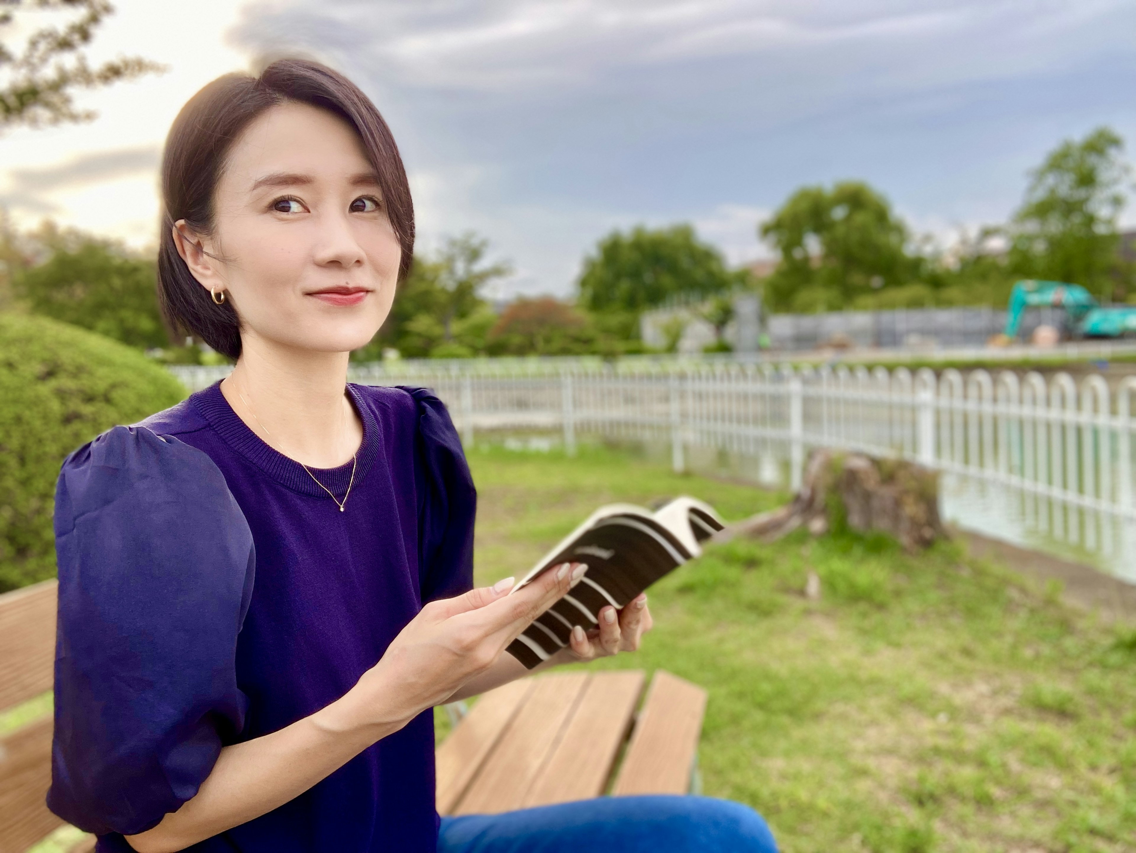 A woman sitting on a park bench holding a book with a smile