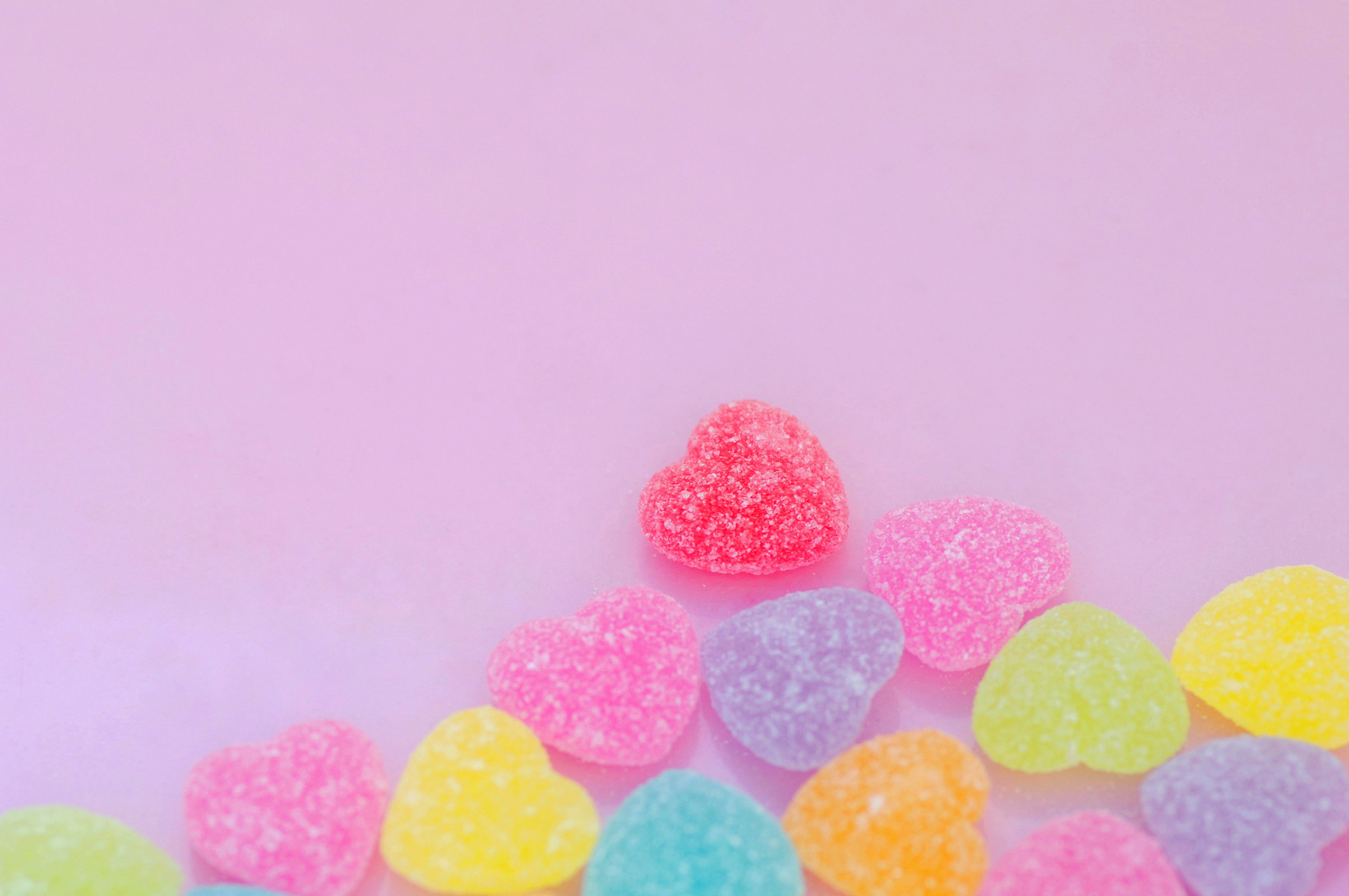 Dulces en forma de corazón coloridos esparcidos sobre un fondo rosa