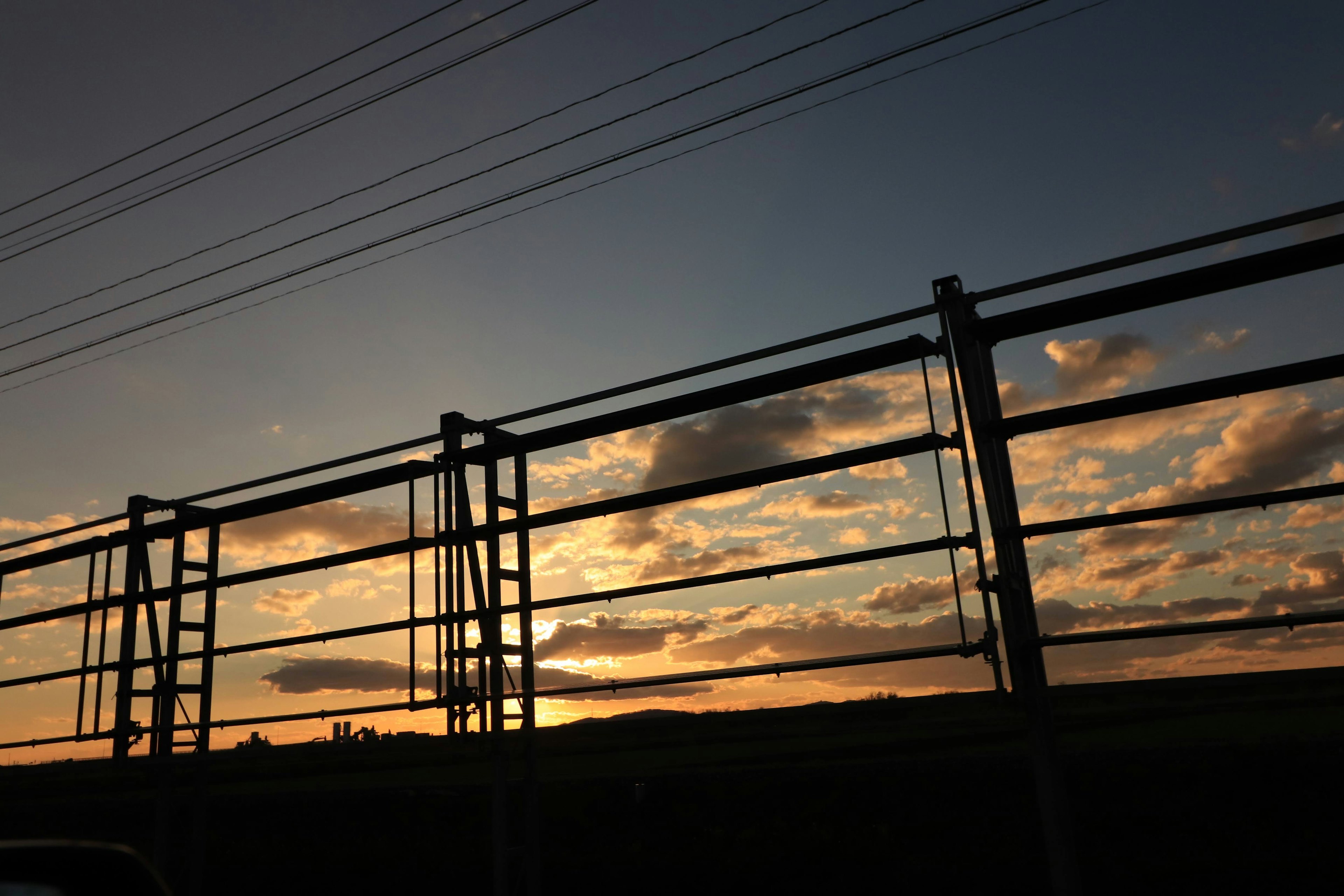 Landschaft mit Sonnenuntergangshimmel und Metallzaun