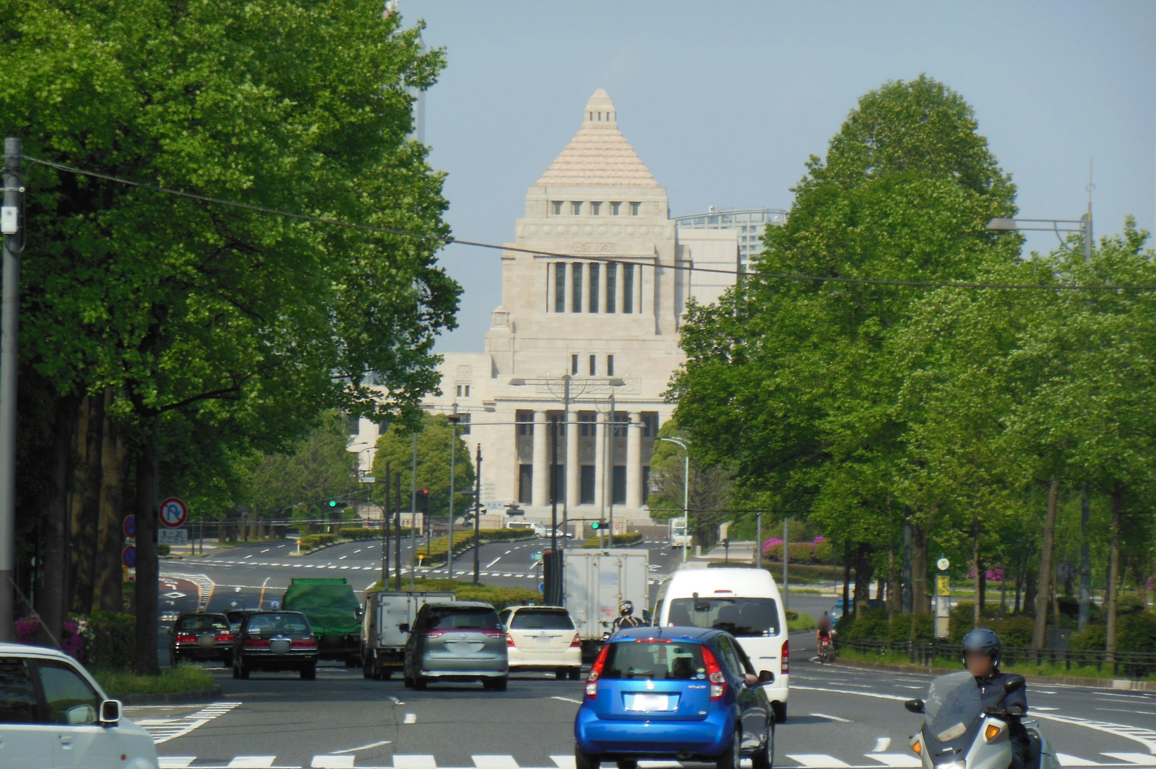 Vista del Edificio del Dieta Nacional con un coche azul y árboles verdes a lo largo de la calle