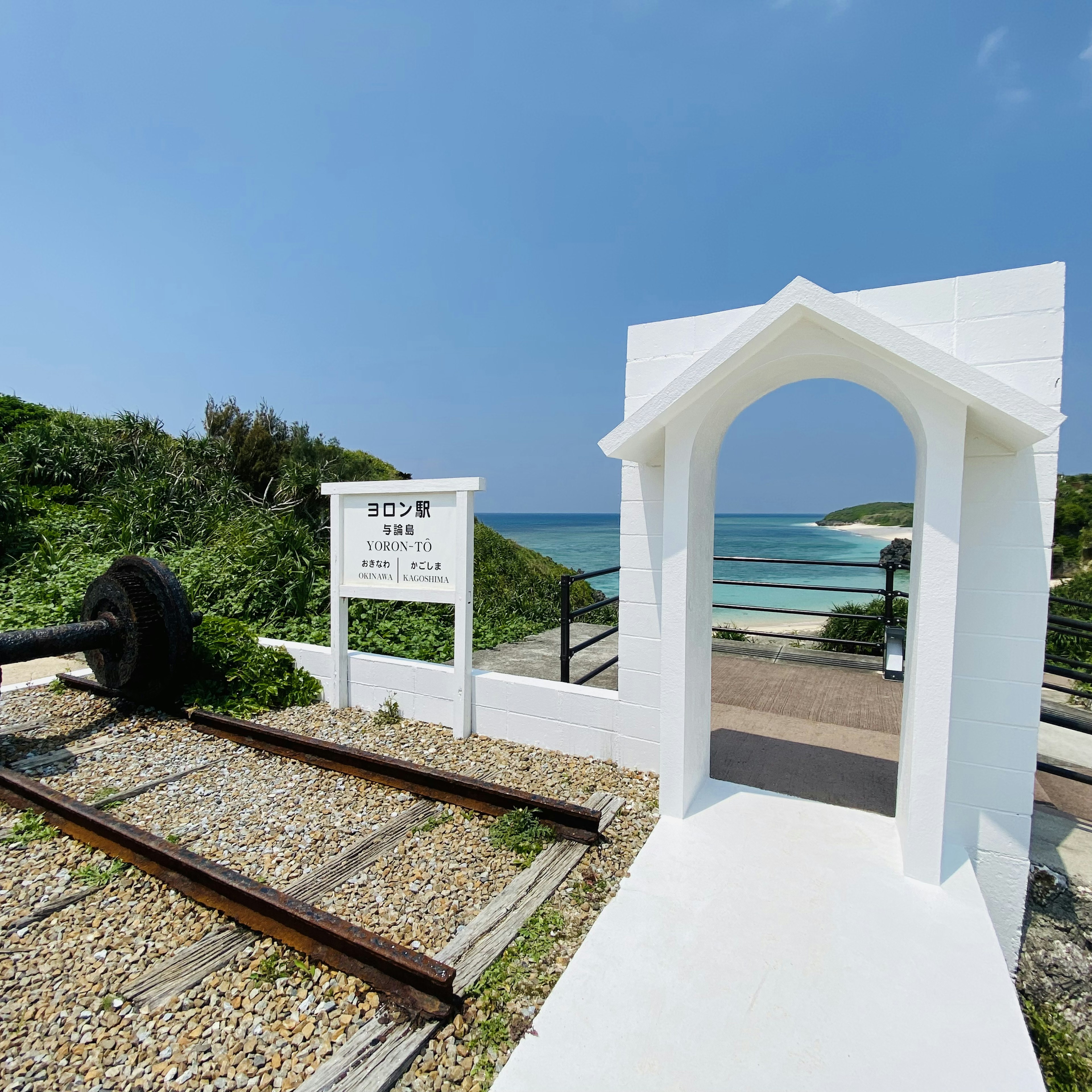 Arco bianco che conduce alla spiaggia con binari