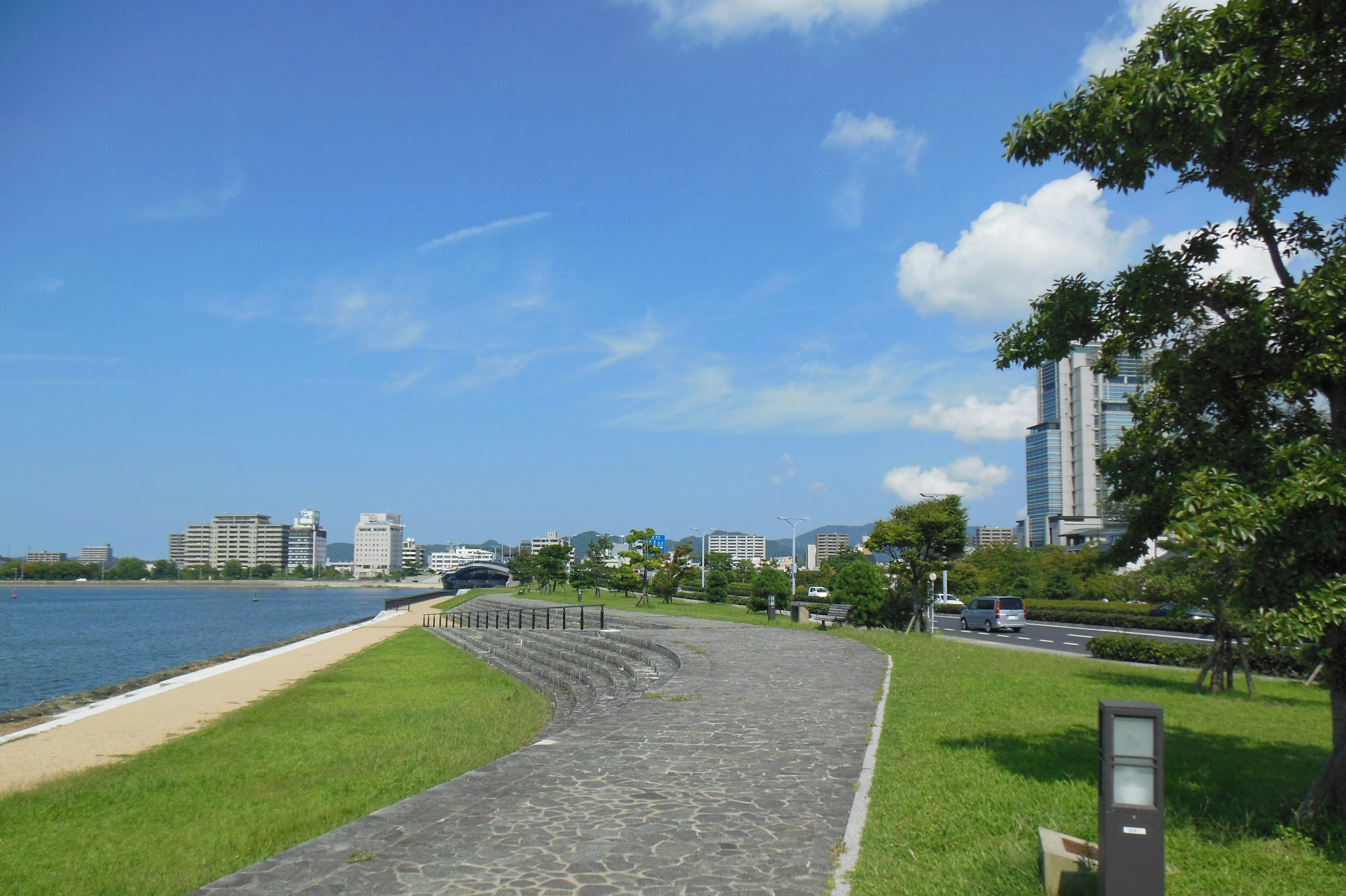 Vista escénica de un paseo junto al río bajo un cielo azul con rascacielos y vegetación exuberante