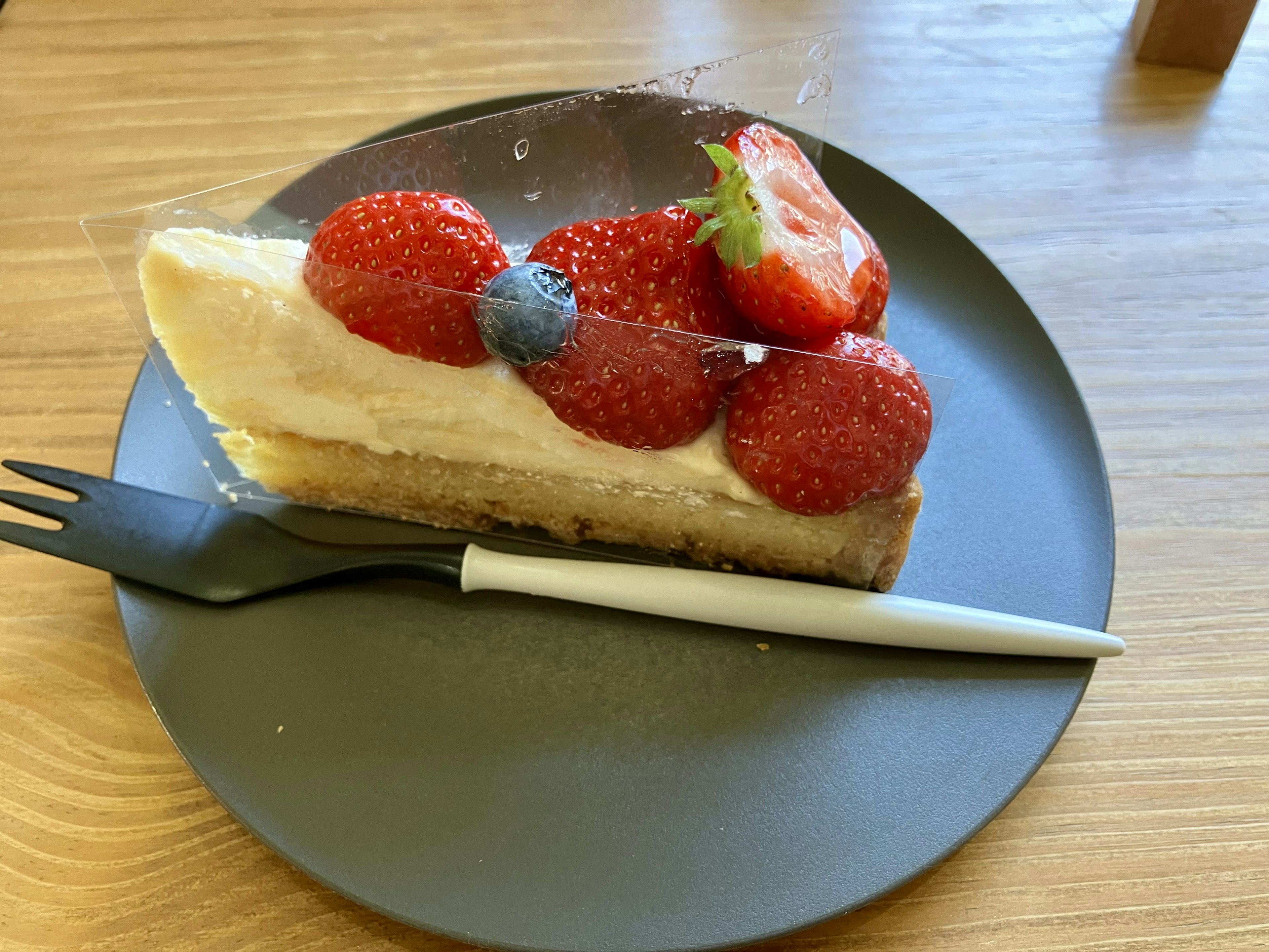 ストロベリーとブルーベリーがトッピングされたクリーミーなケーキが黒い皿に載っている