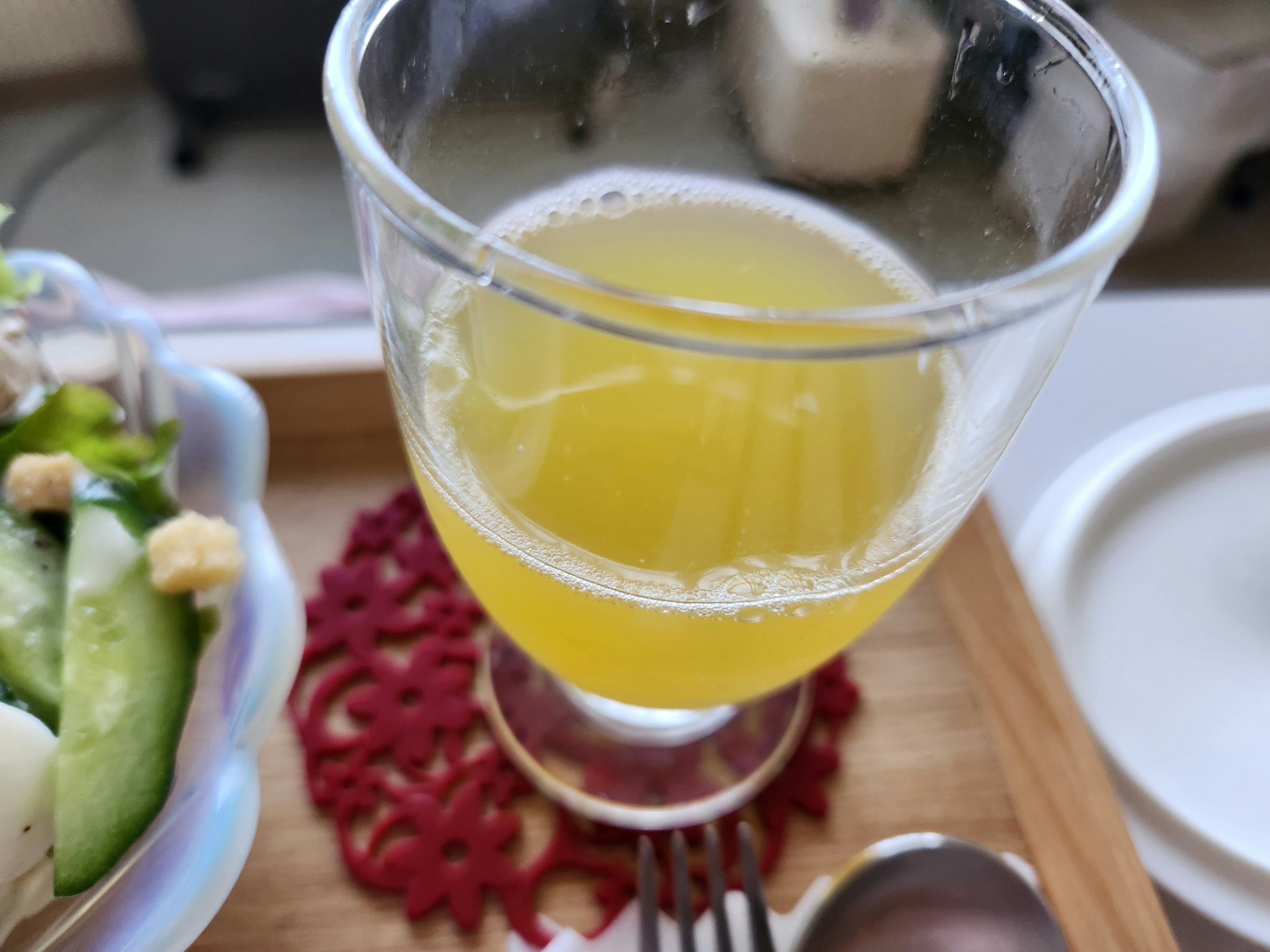 Un vaso transparente que contiene una bebida amarilla junto a una ensalada en una bandeja