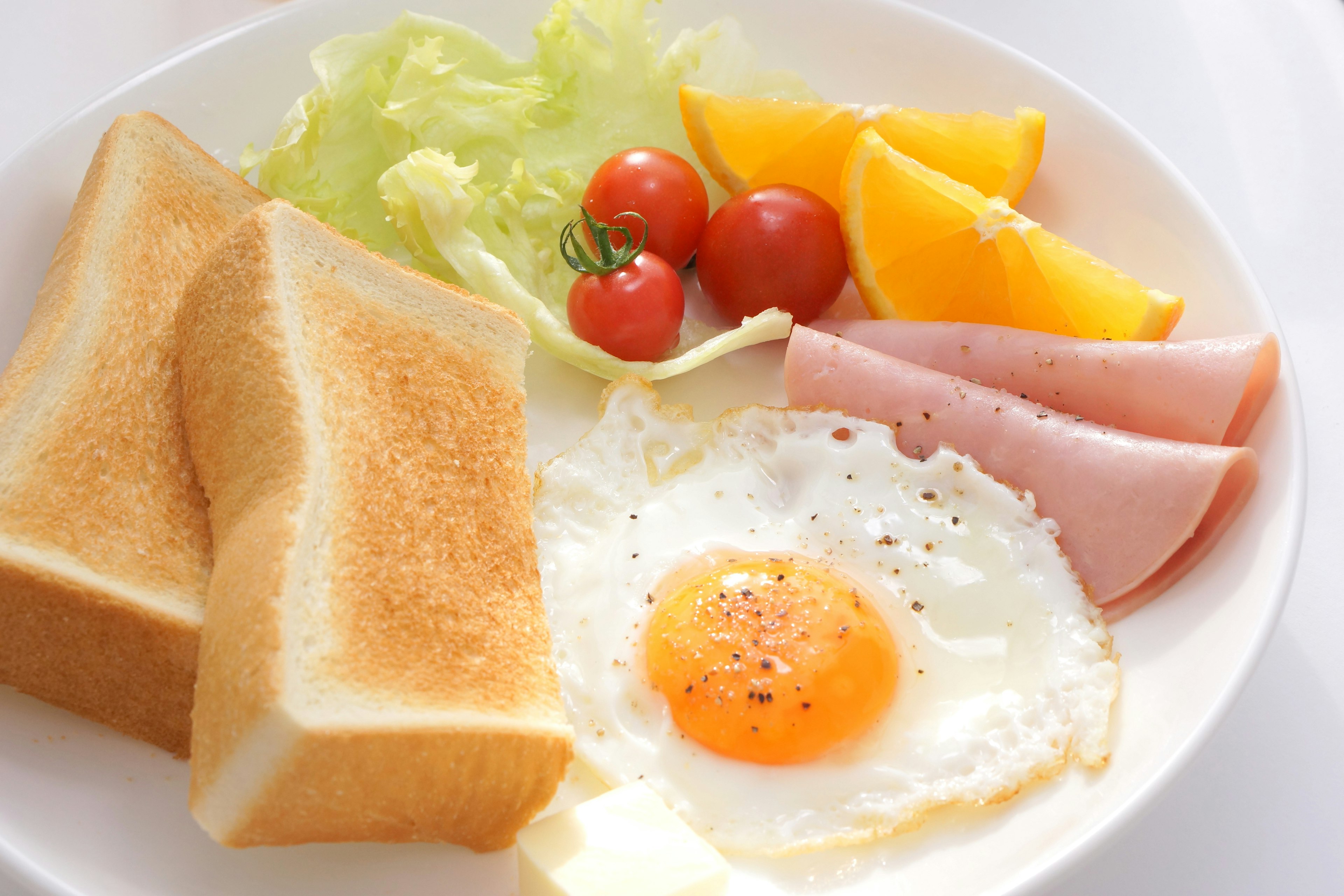 Breakfast plate with toast, fried egg, ham, salad, cherry tomatoes, and orange slices