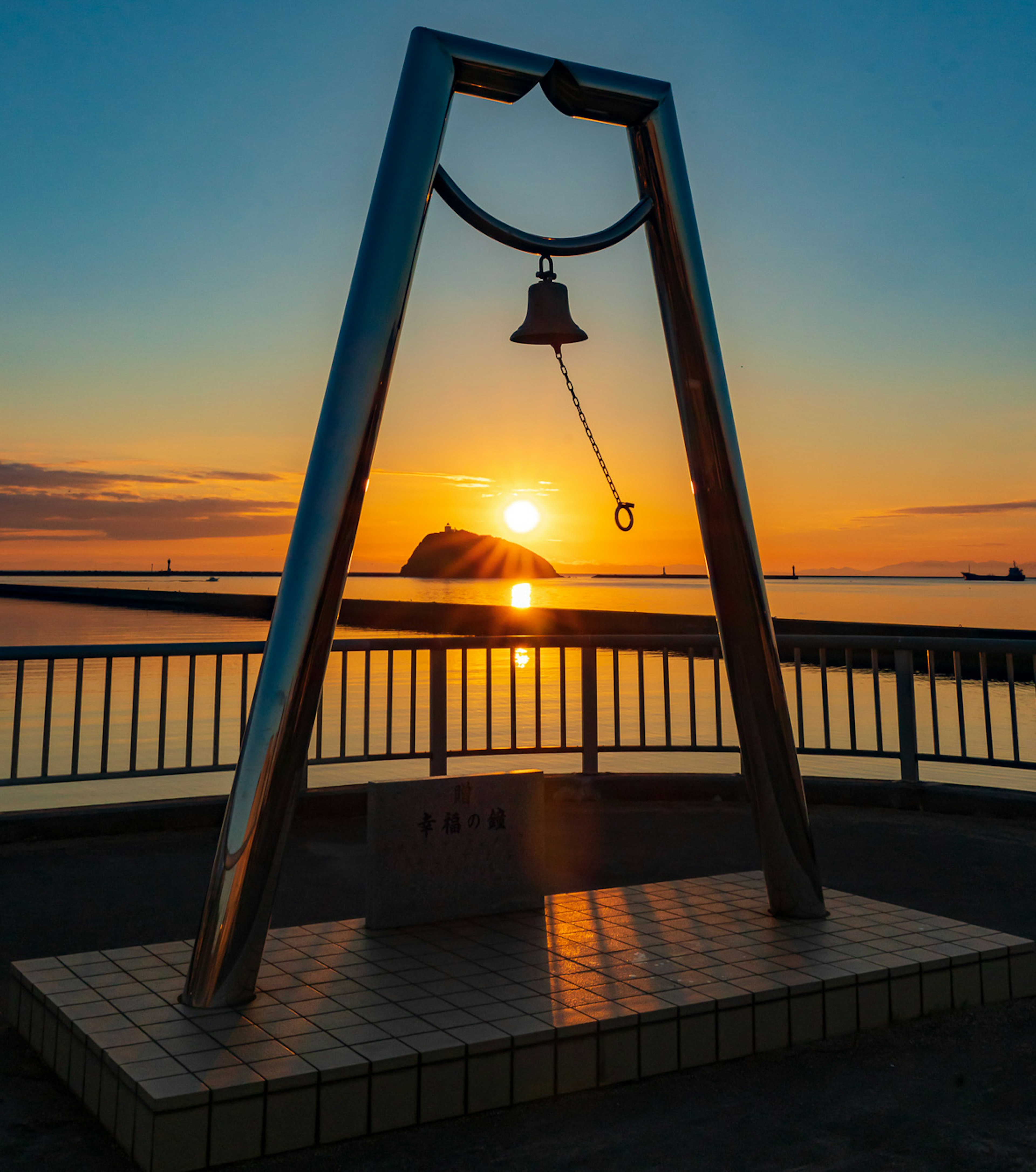 夕日を背にした鐘のモニュメントが海に映る美しい風景