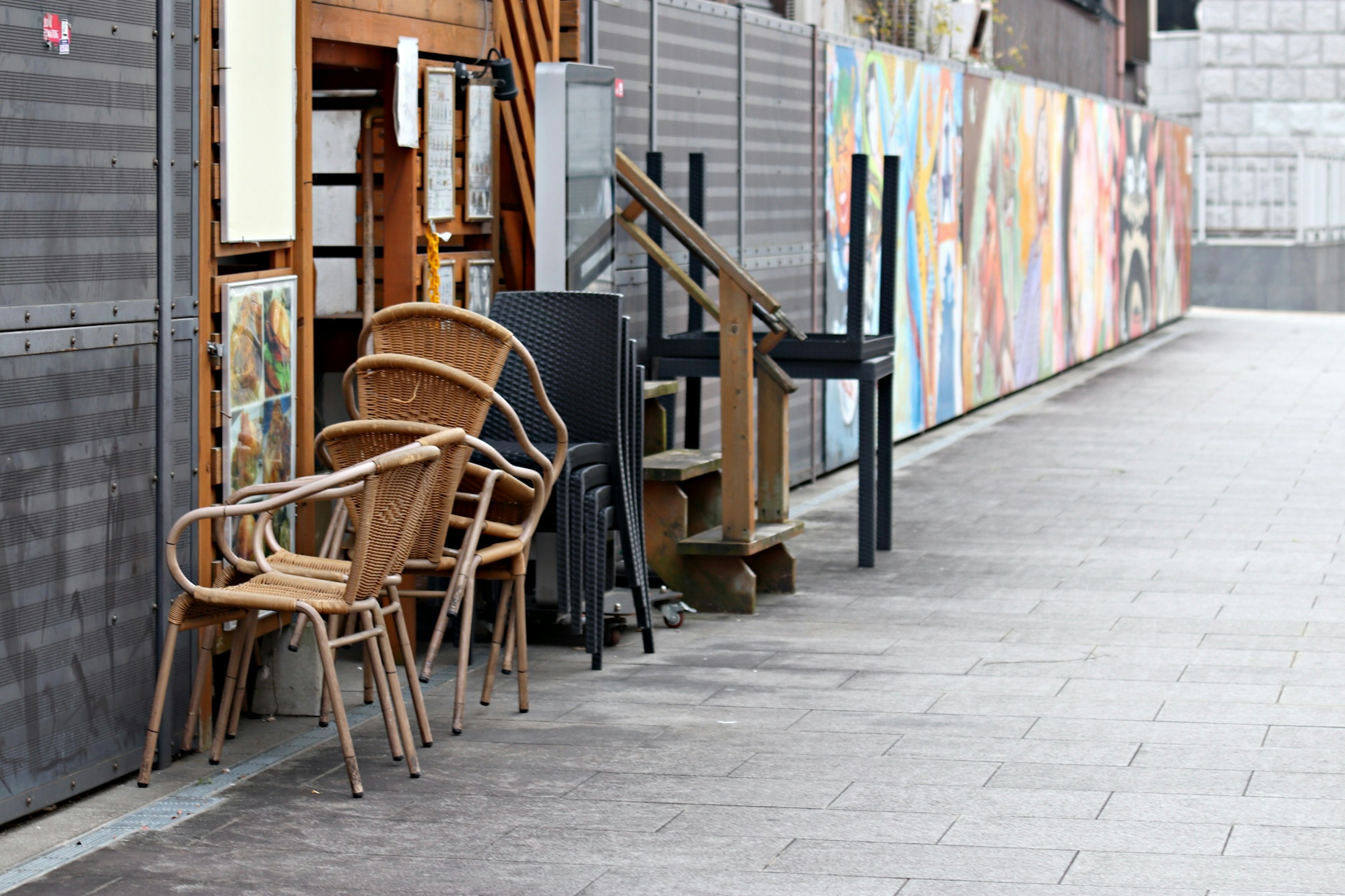 Ensemble de chaises et de table en bois placé sur le trottoir avec des murales colorées en arrière-plan