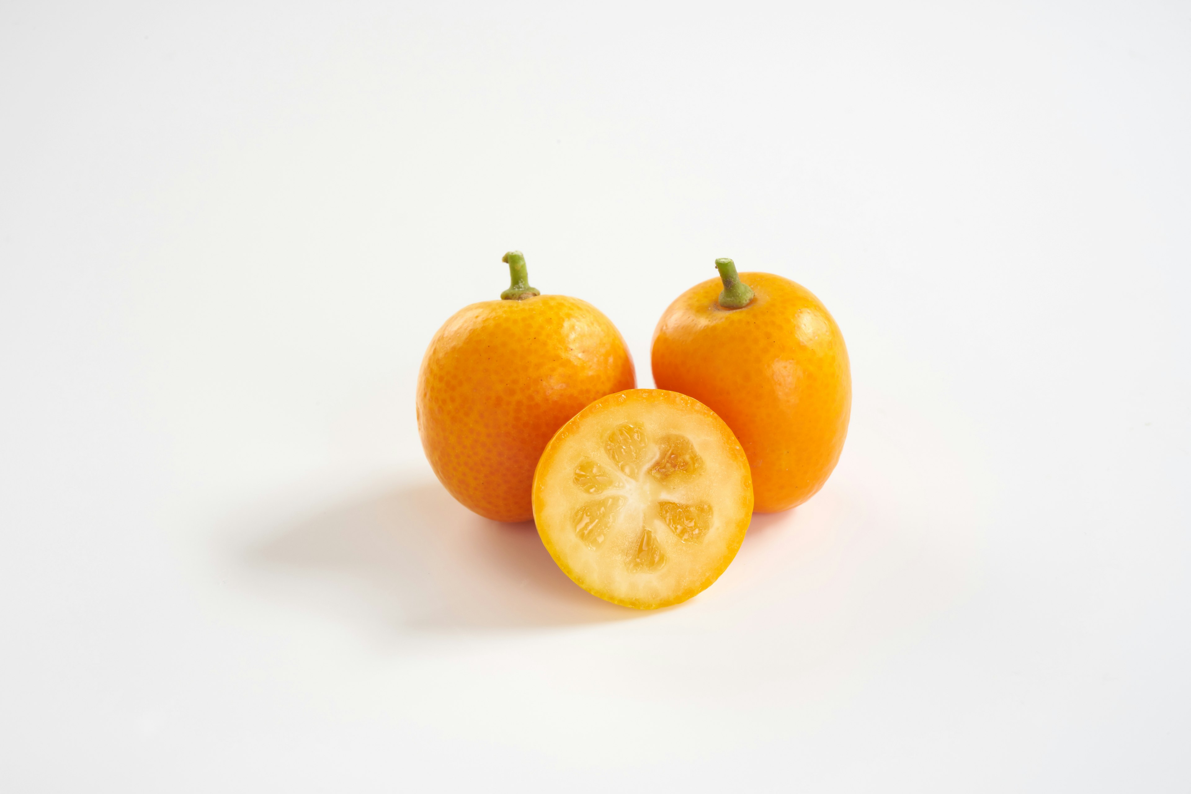 Dos frutas redondas naranjas y una fruta cortada sobre un fondo blanco