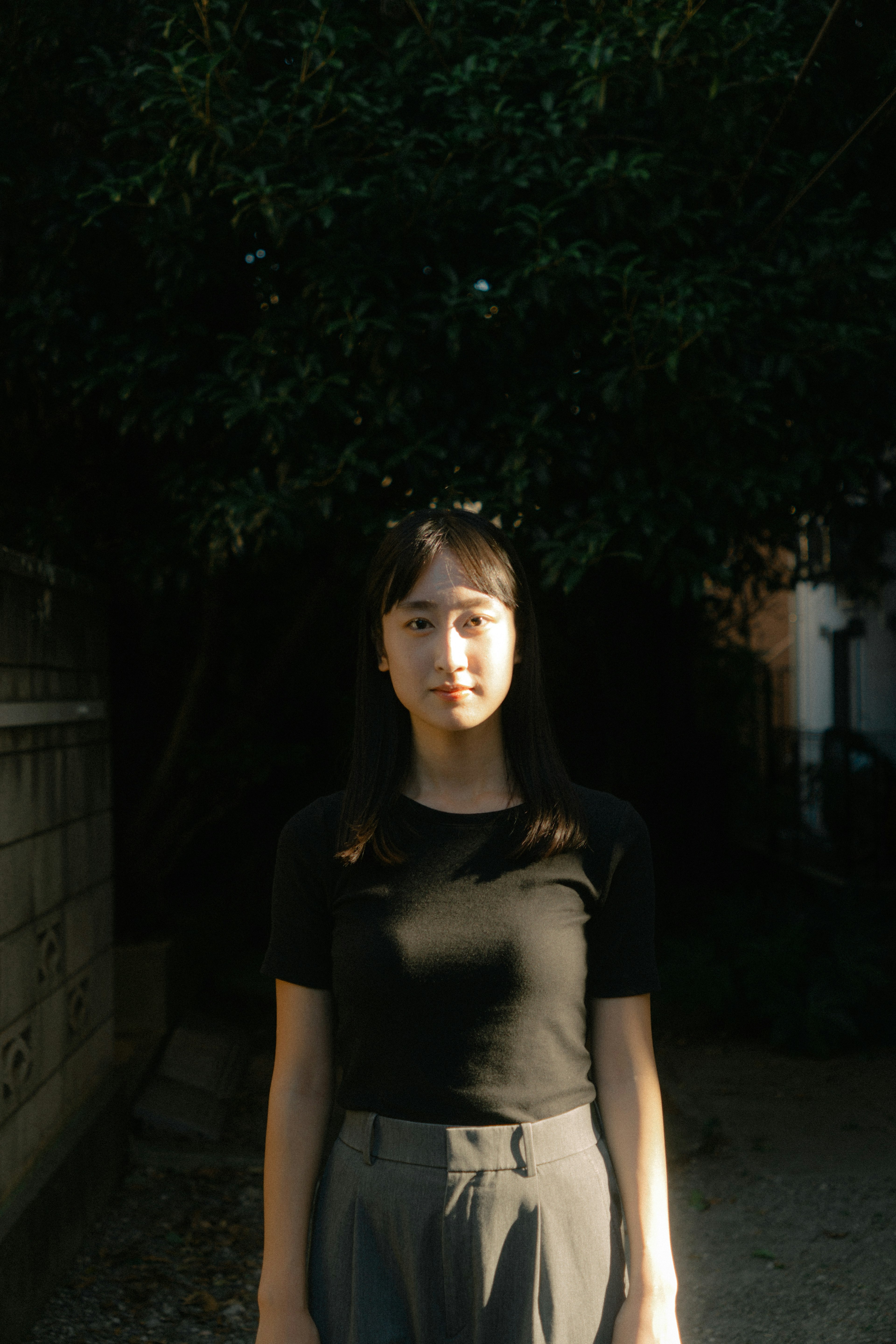 Portrait of a woman standing in front of a dark background wearing a black t-shirt and gray pants