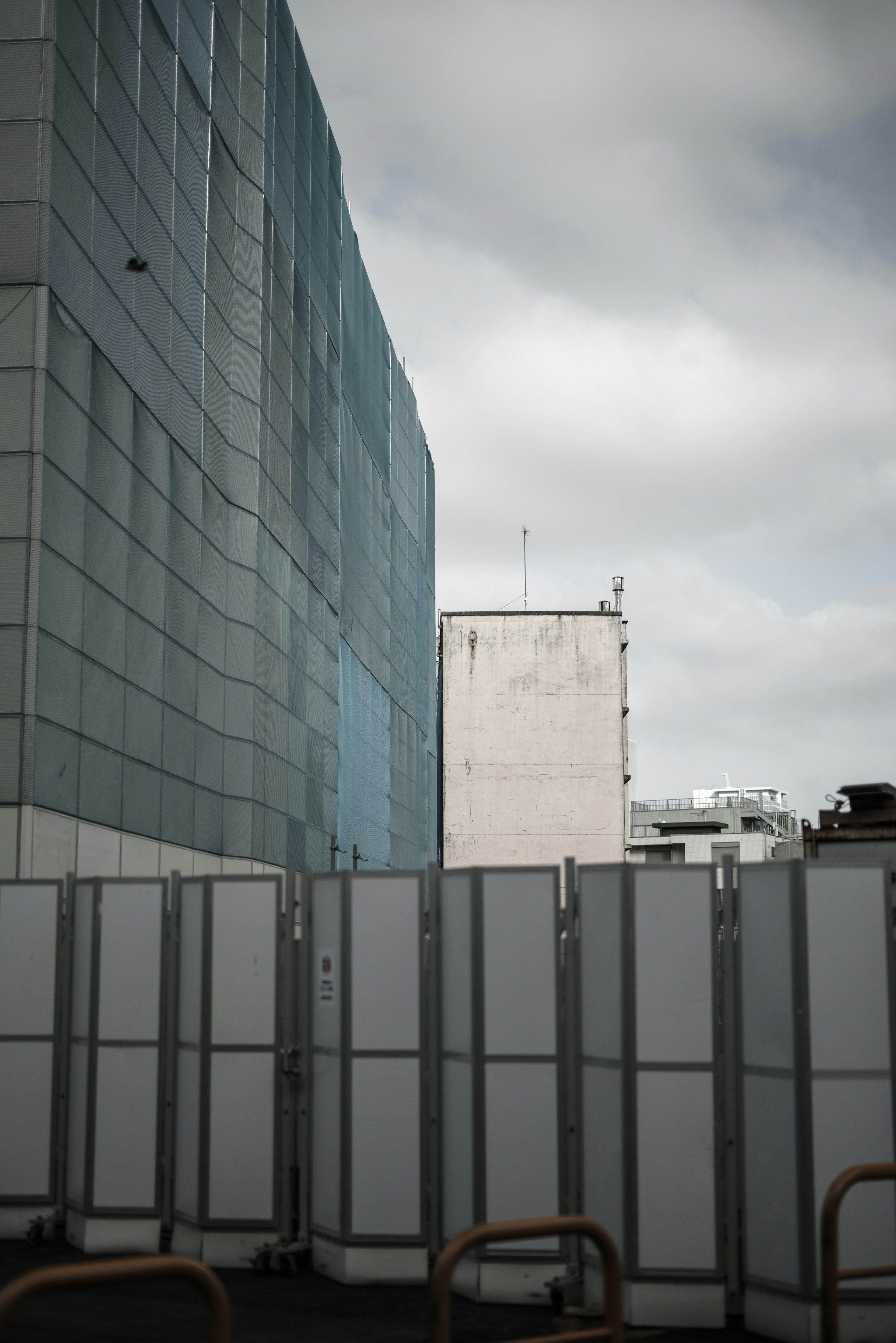 Graue Paneele zwischen einem blauen Glasgebäude und einem weißen Wandgebäude unter bewölktem Himmel