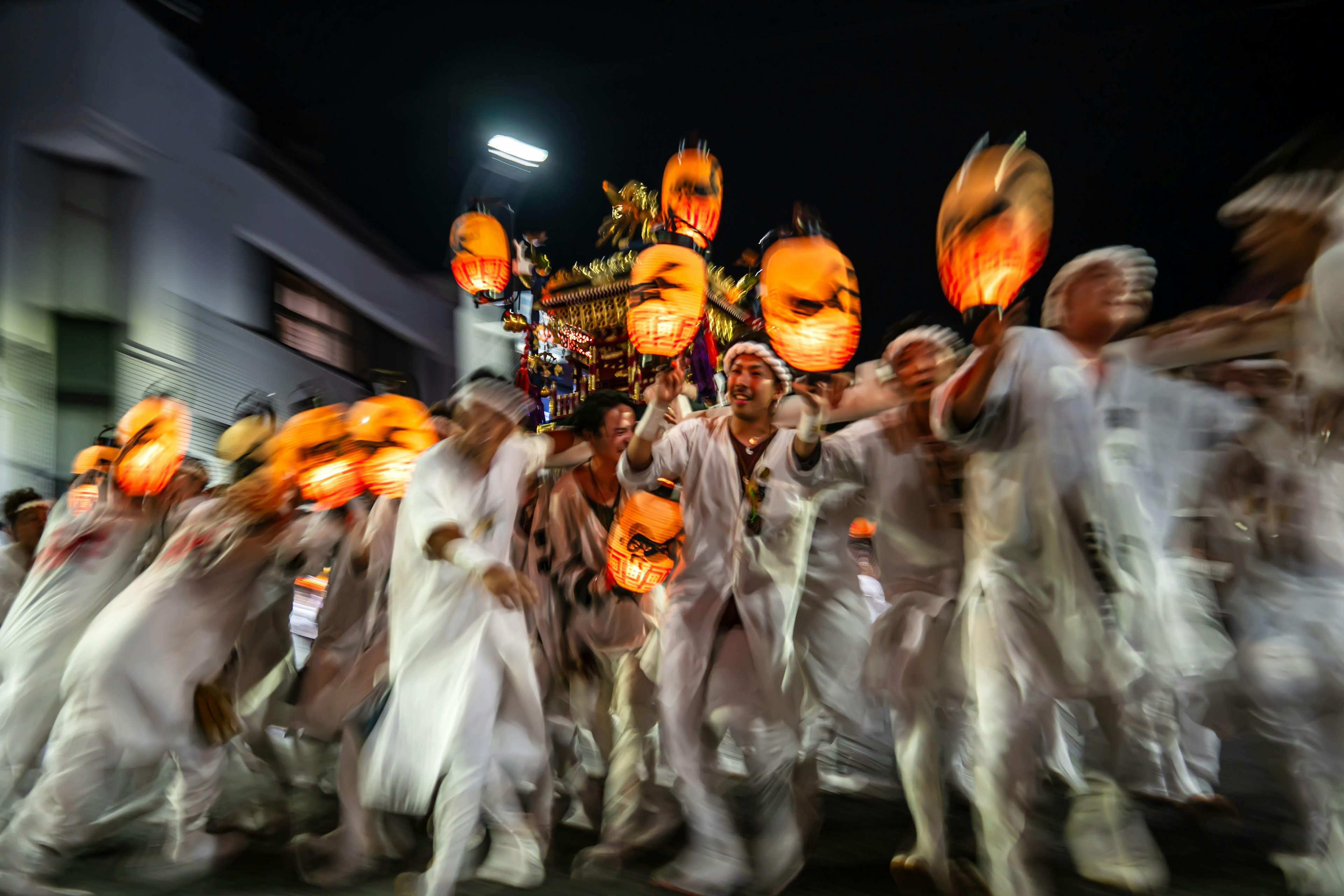 People in white costumes holding orange lanterns during a night festival