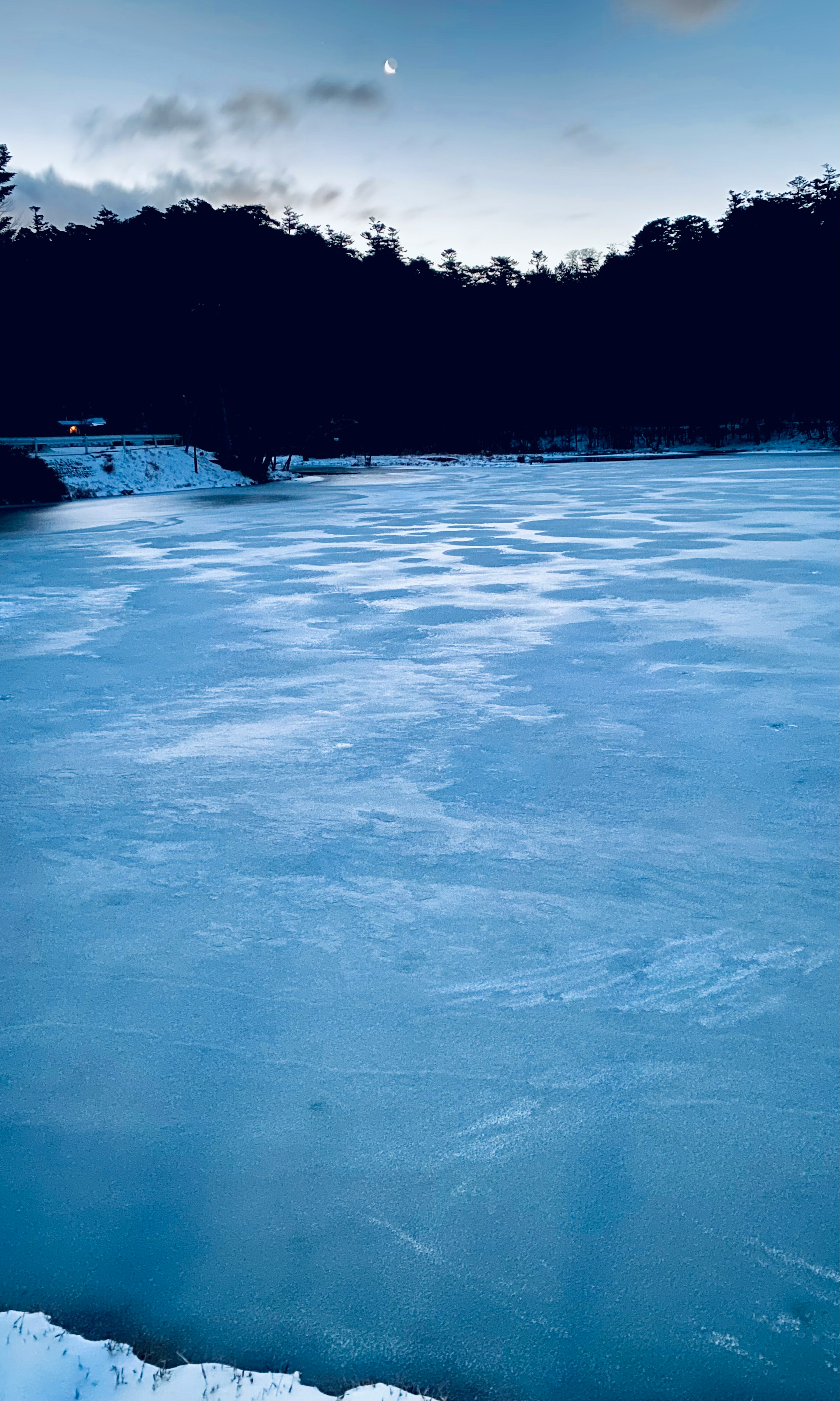 Lago congelado con superficie azul y silueta de árboles a lo lejos