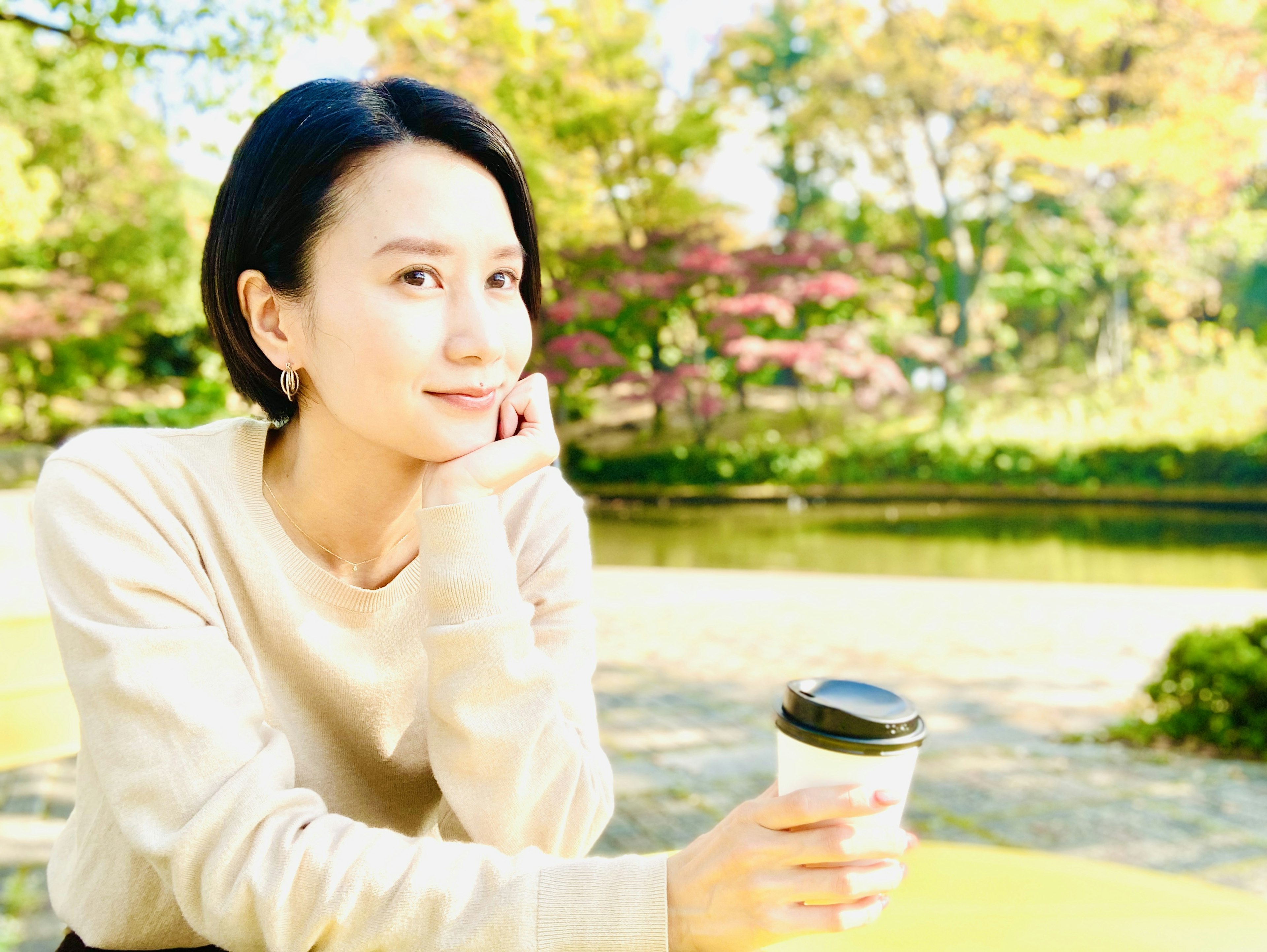 Retrato de una mujer sonriendo mientras sostiene un café en un parque