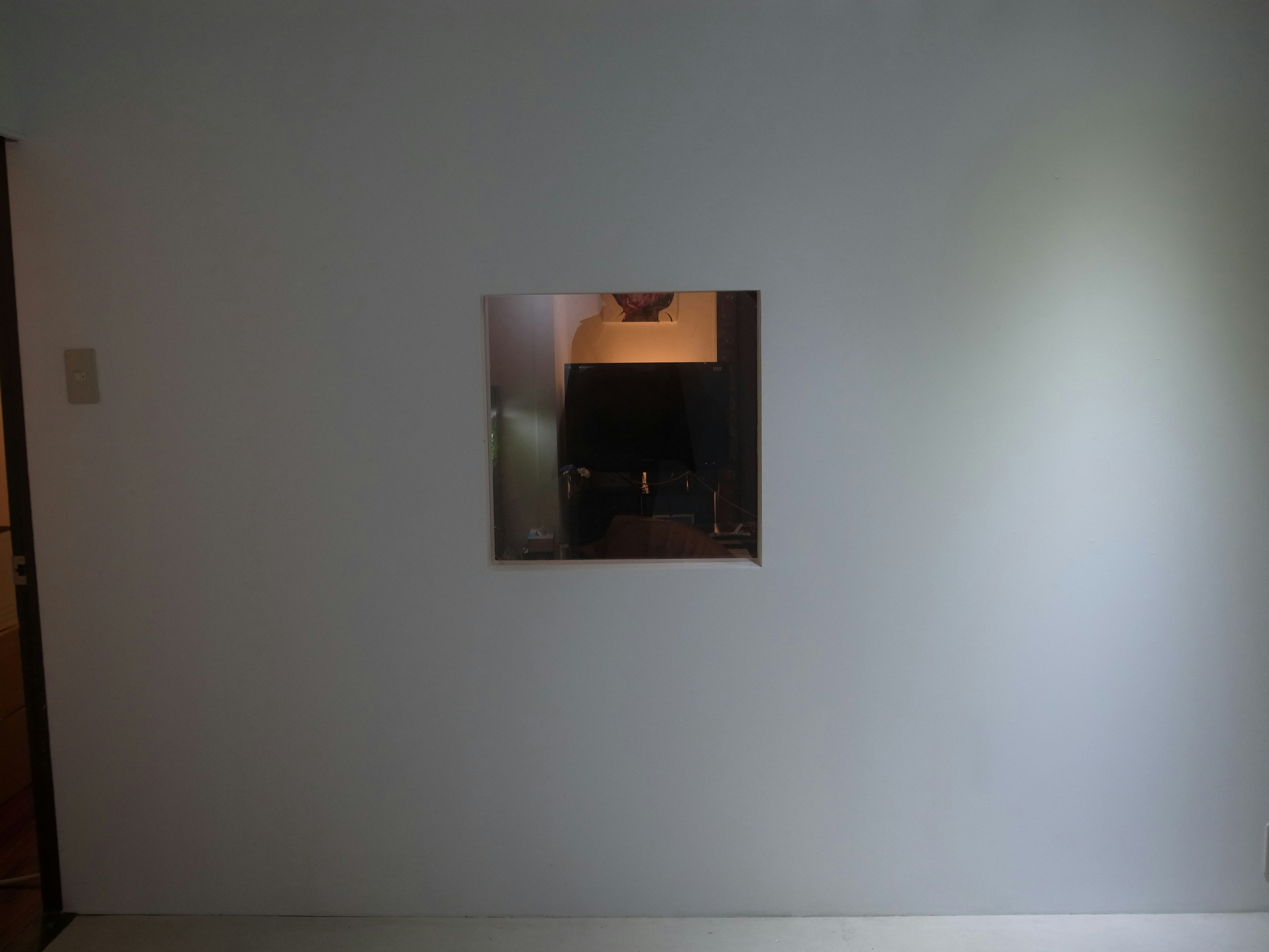 Square mirror mounted on a white wall reflecting part of a room