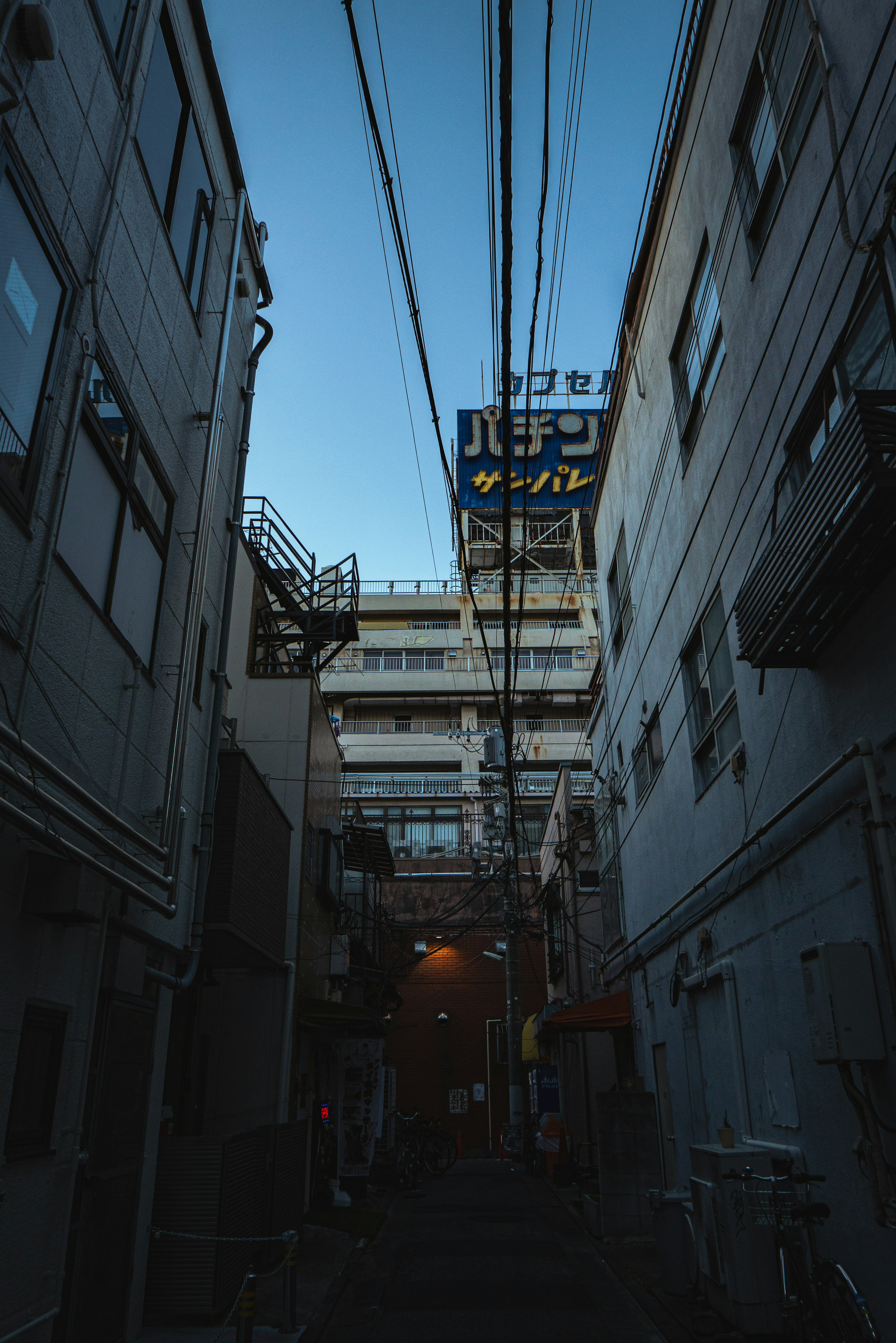 Callejón estrecho con edificios y líneas eléctricas bajo un cielo crepuscular