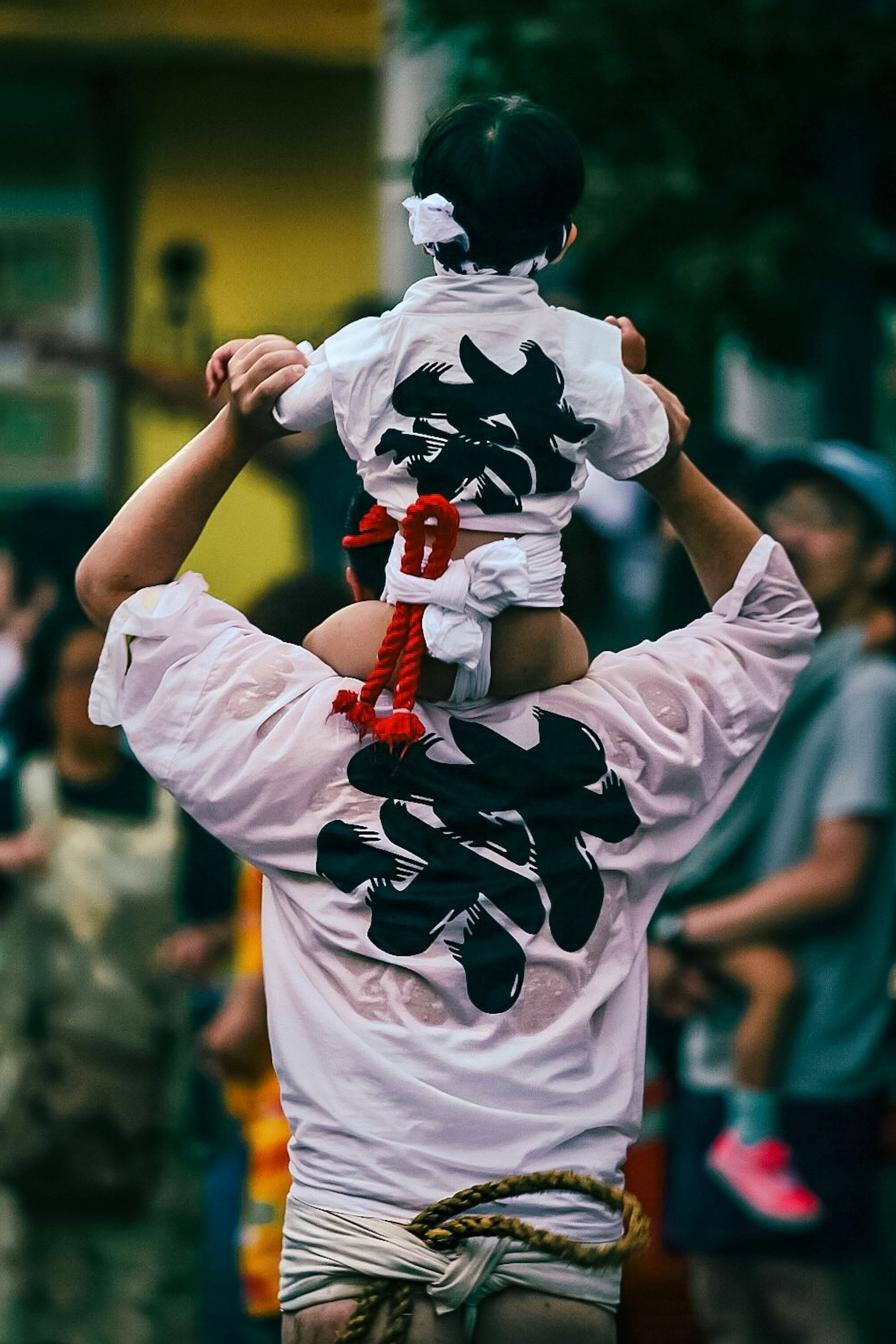 A man carrying a child on his shoulders wearing traditional festival attire