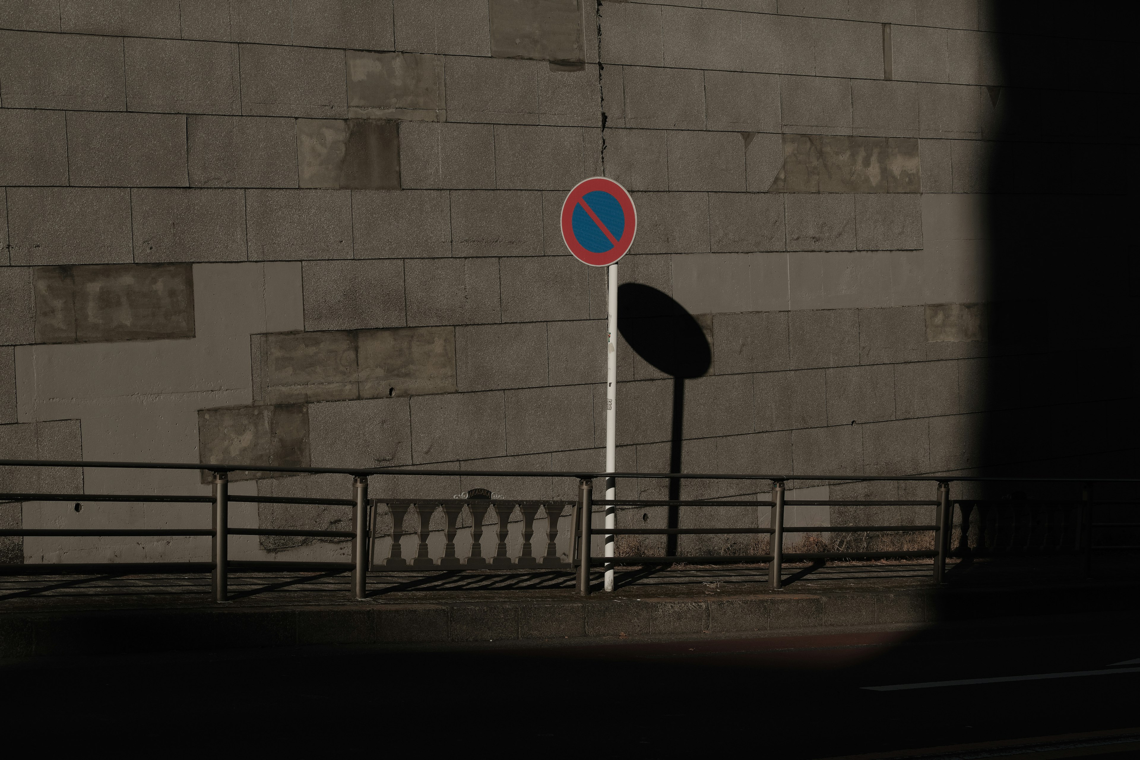 No parking sign standing against a dark wall with a shadow