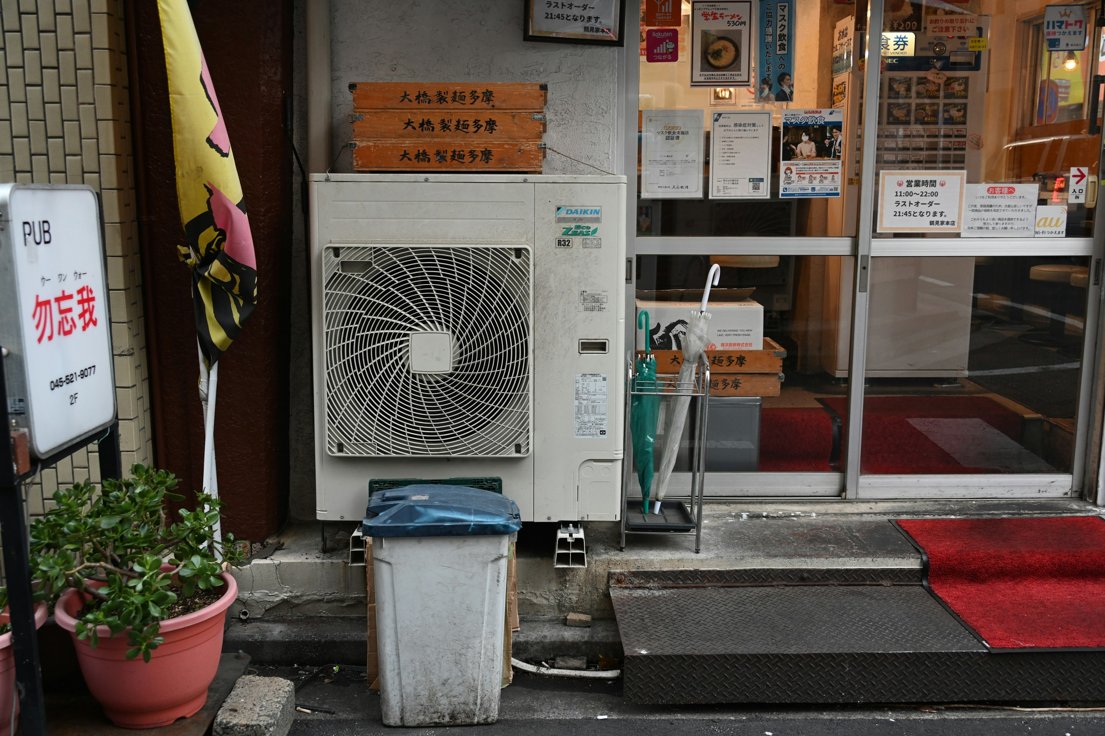 Vista exterior de una tienda con una unidad de aire acondicionado y un basurero cerca de la entrada