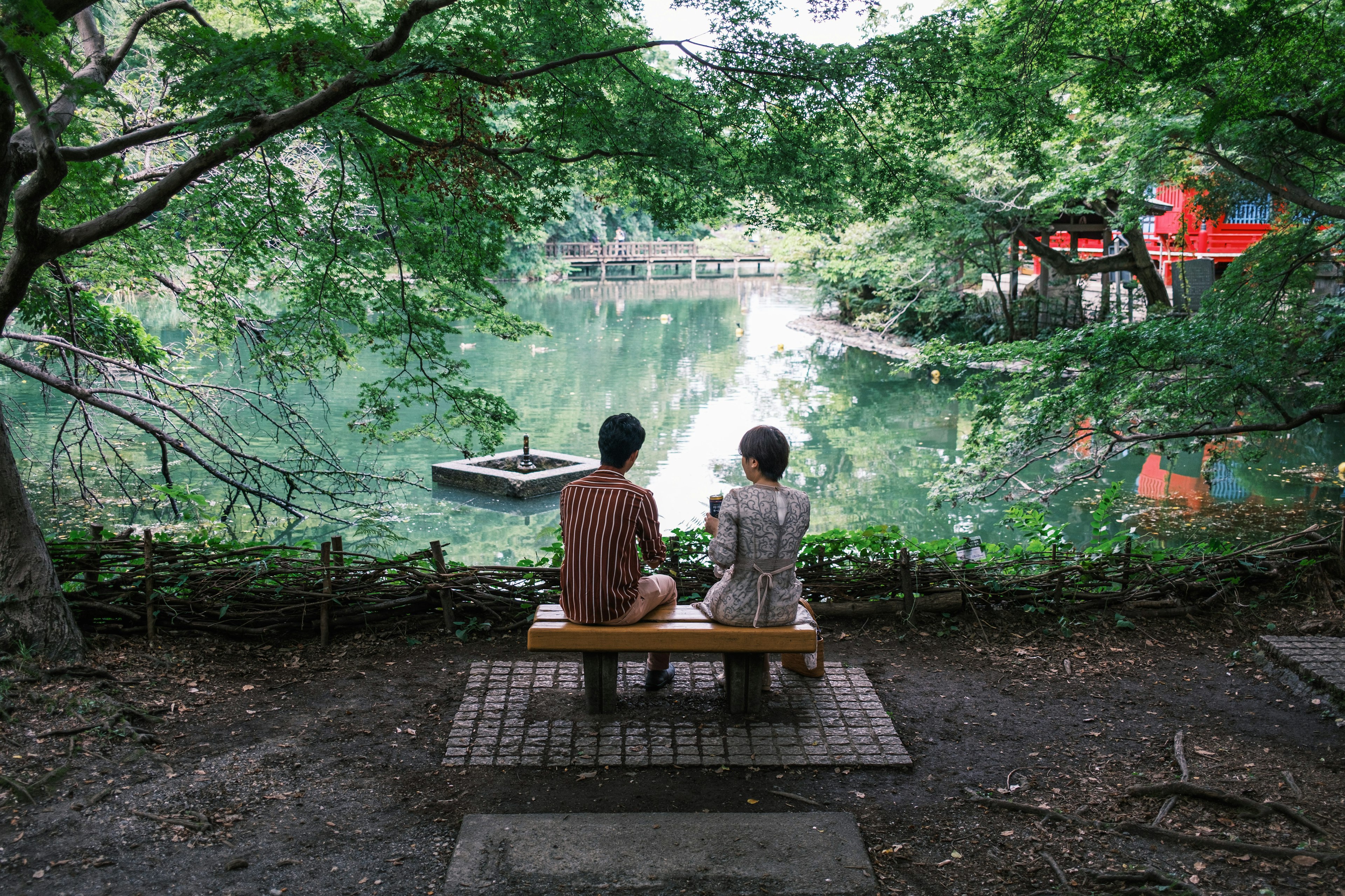 静かな池のほとりでベンチに座る二人の人物