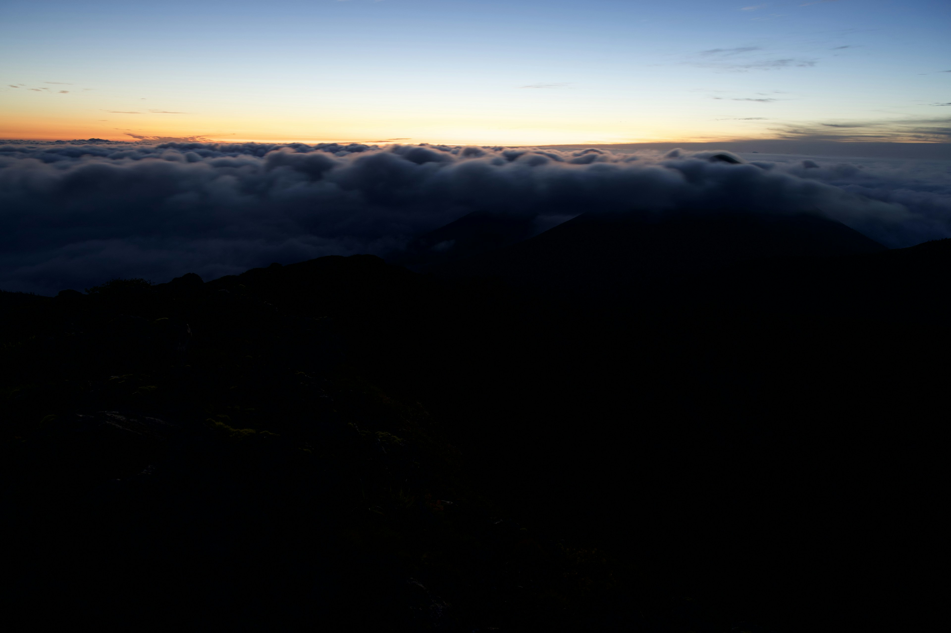 Cielo blu con tramonto arancione sopra un mare di nuvole