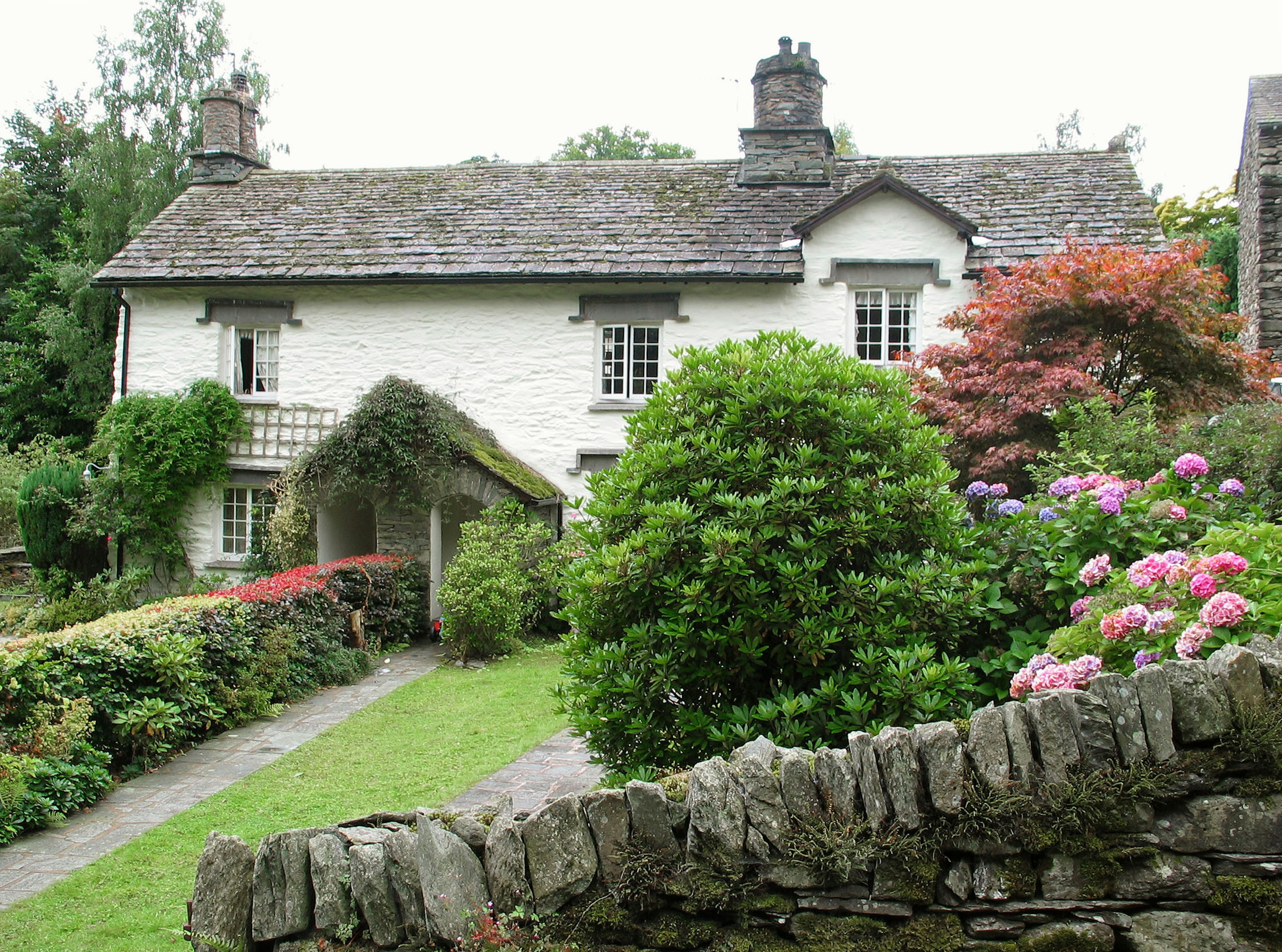 Charming white cottage surrounded by lush garden and stone wall