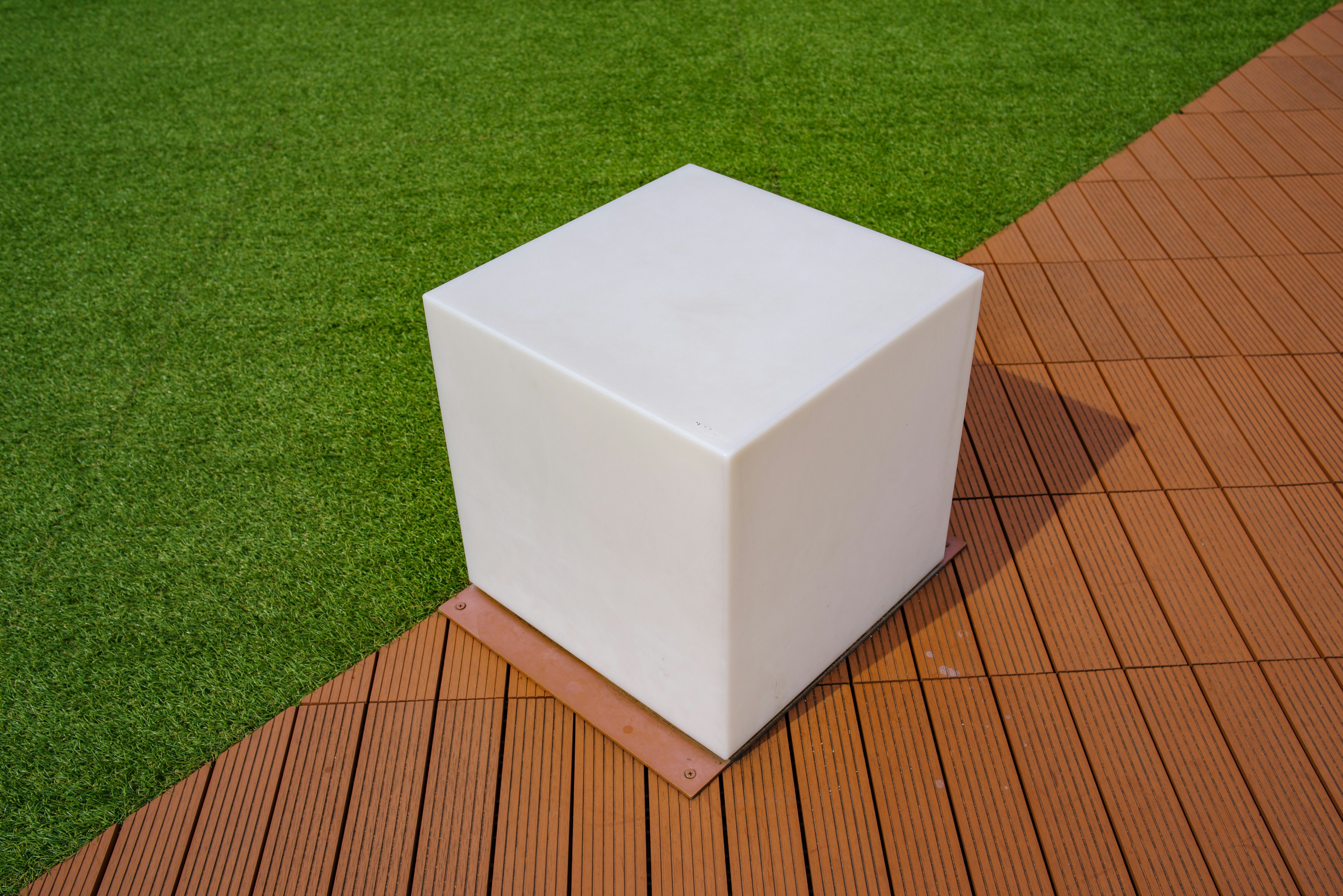 A white cube placed on green grass next to a wooden deck